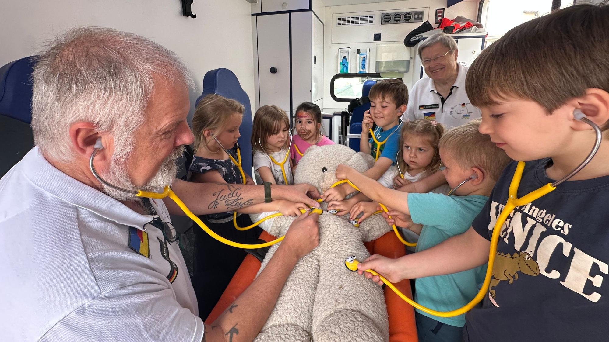 Der Verein Sankt Augustin hilft erklärt Kindern aus der Kita Bismarckplatz wie ein Rettungswagen funktioniert. Gunter Maassen (l.) erklärt die Funktionsweise eines Stethoskops.