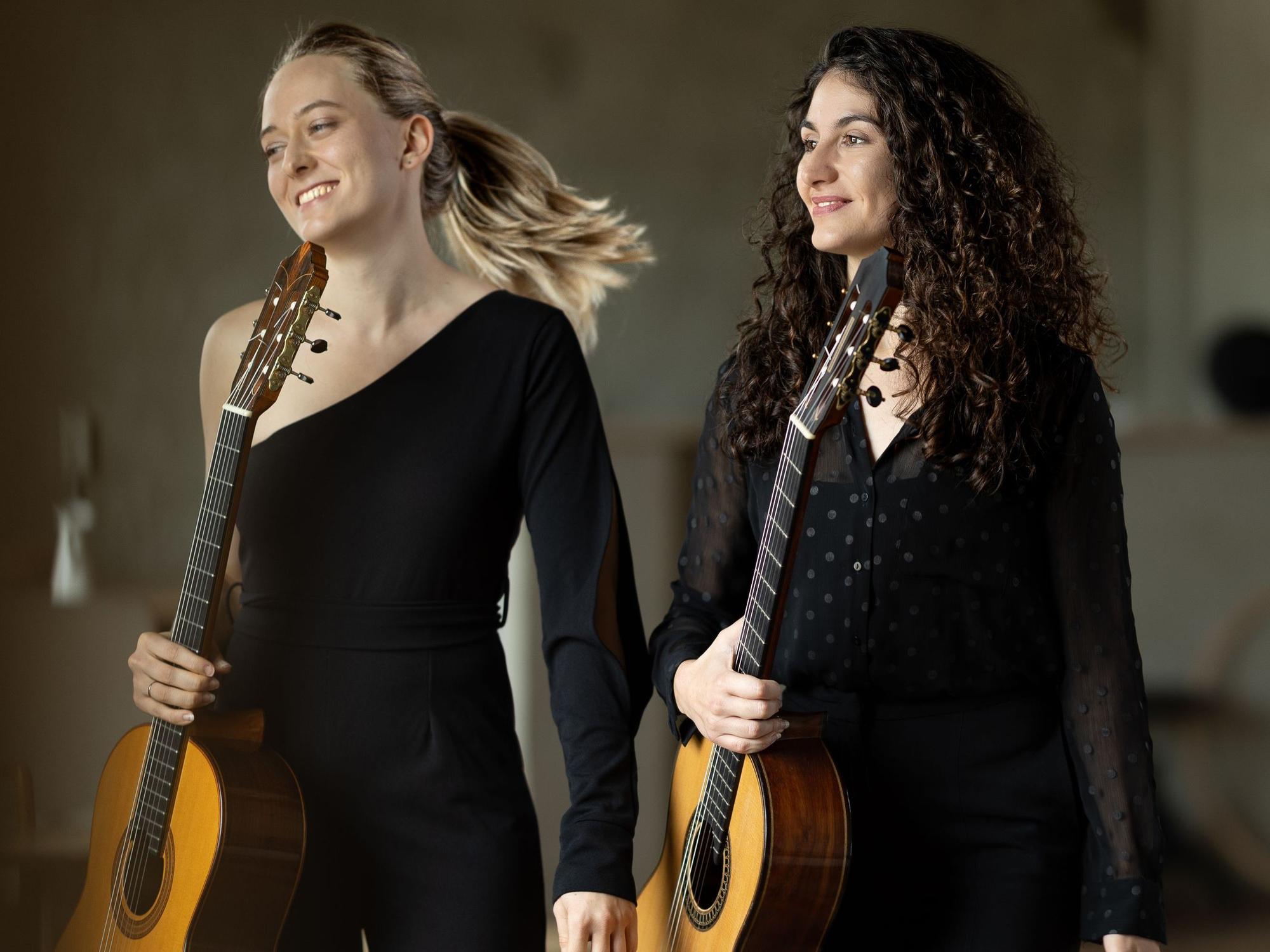 Ana Cižmek (l.) und Petra Stojakovic stehen nebeneinander, halten Gitarren und schauen auf etwas außerhalb des Bildbereichs.