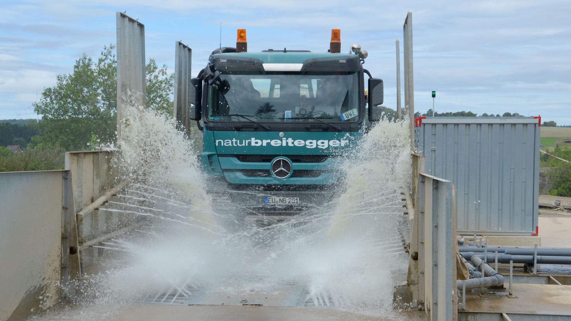Ein Lastwagen fährt durch die Anlage. Zahlreiche Wasserfontänen sind zu sehen.