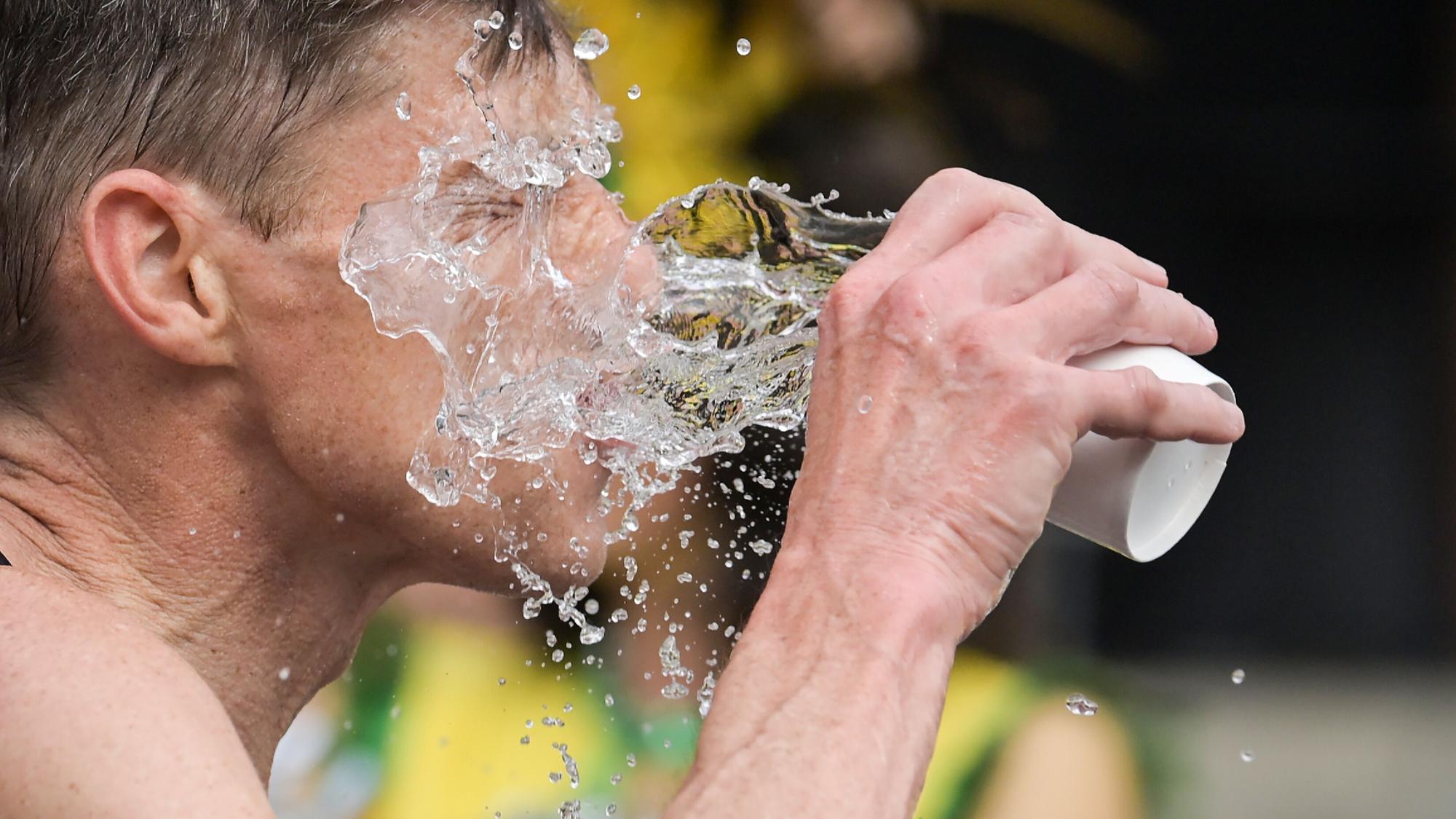 Ein Mann, vermutlich ein Sportler, schüttet sich einen Becher Wasser ins Gesicht.