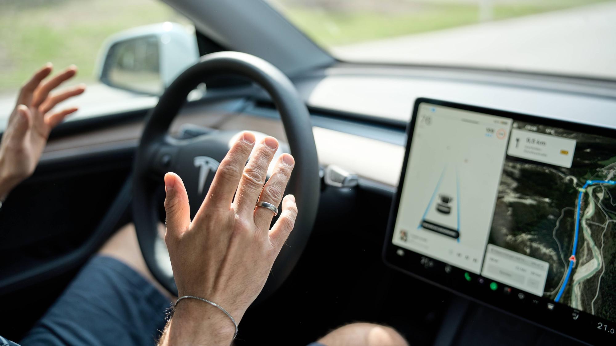 Ein Autofahrer nimmt in einem Tesla die Hände vom Steuer - das Auto lenkt autonom durch den Verkehr.