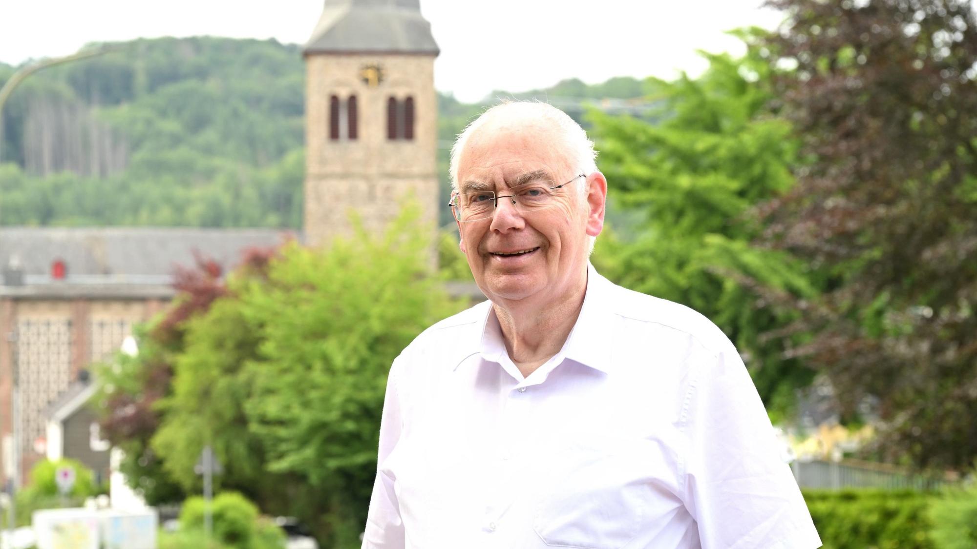 Zu sehen ist ein älterer Mann, der in einiger Entfernung zu einem Kirchturm steht.