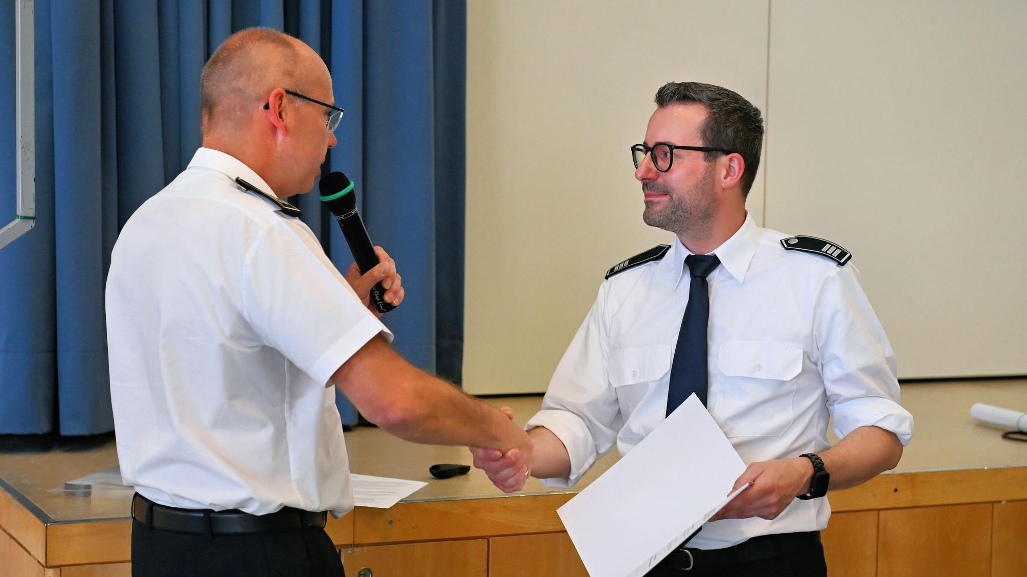 Zwei Feuerwehrleute in weißen Uniform-Hemden geben sich die Hand.