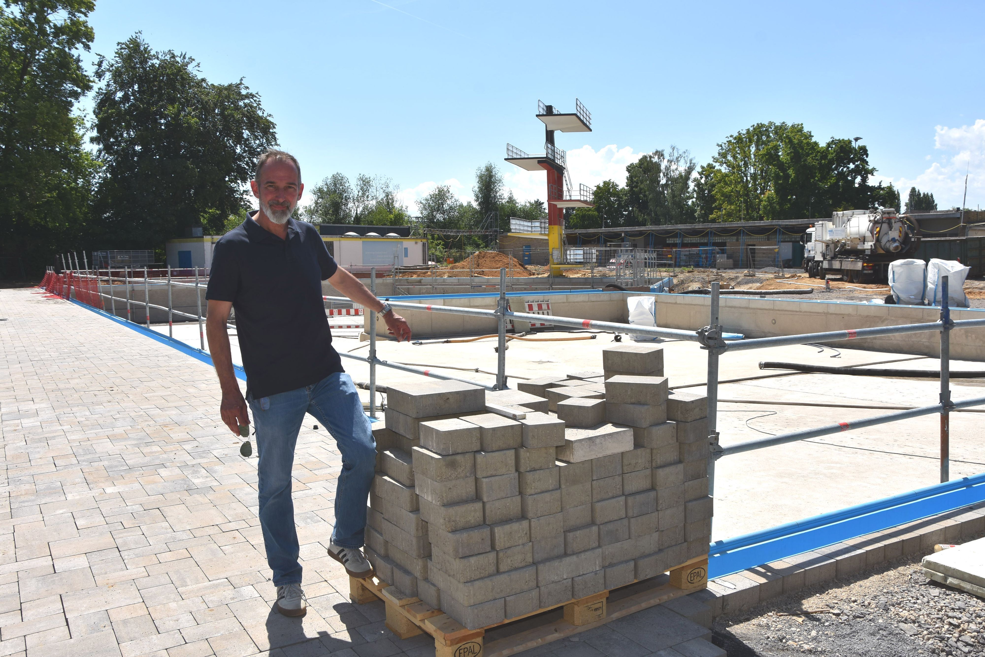 Ein Mann steht vor der Baustelle eines Schwimmbads.