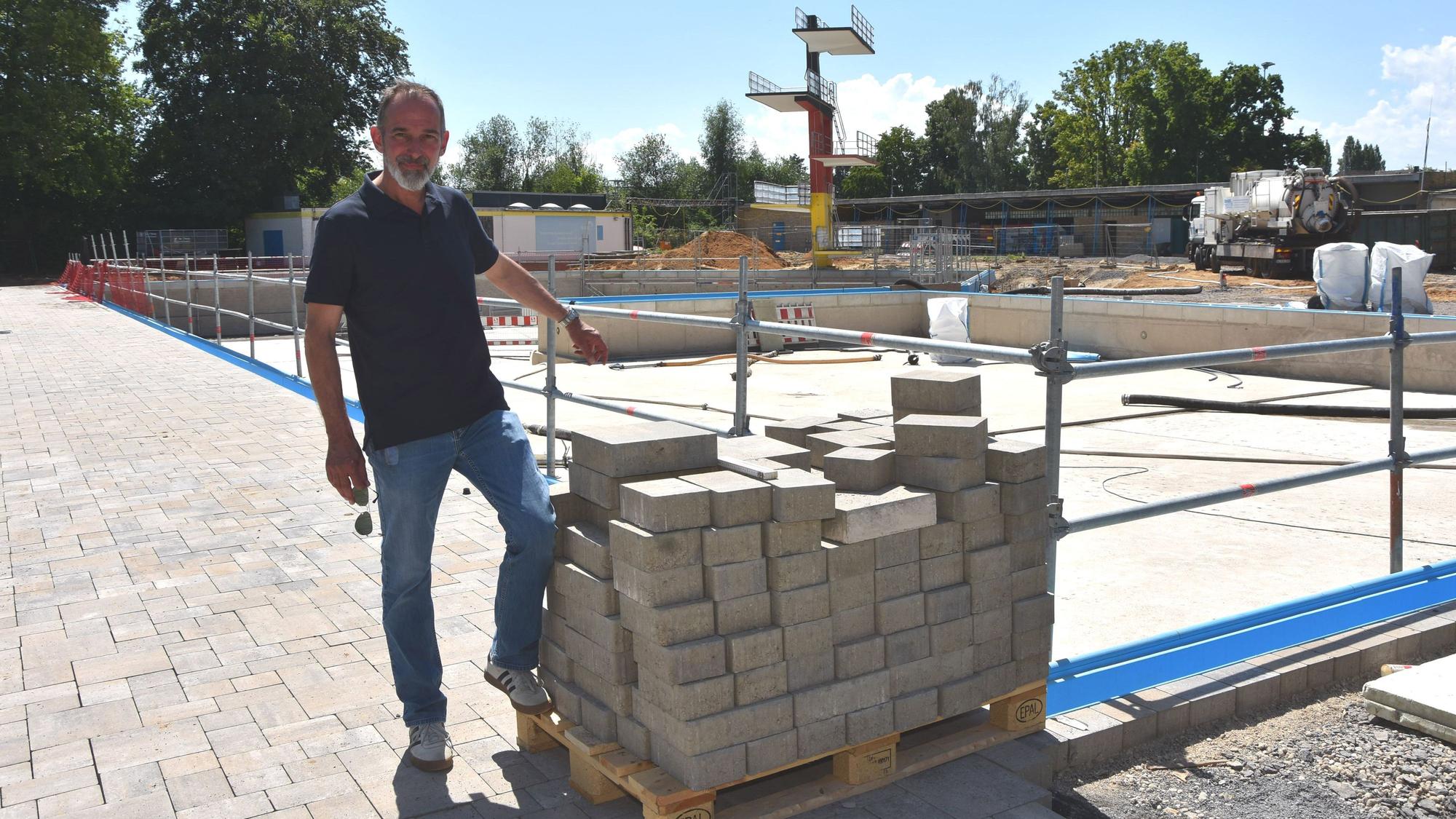 Ein Mann steht vor der Baustelle eines Schwimmbads.