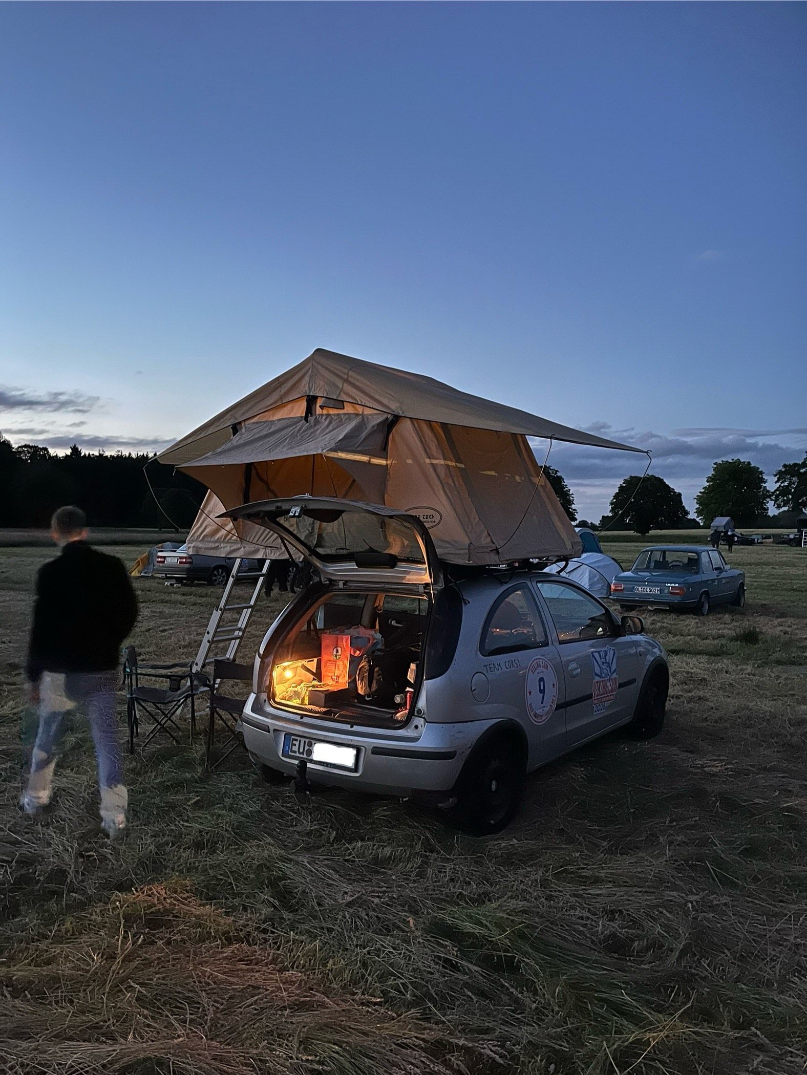 Das Auto steht auf einer Wiese, das Dachzelt mit Leiter ist aufgestellt.