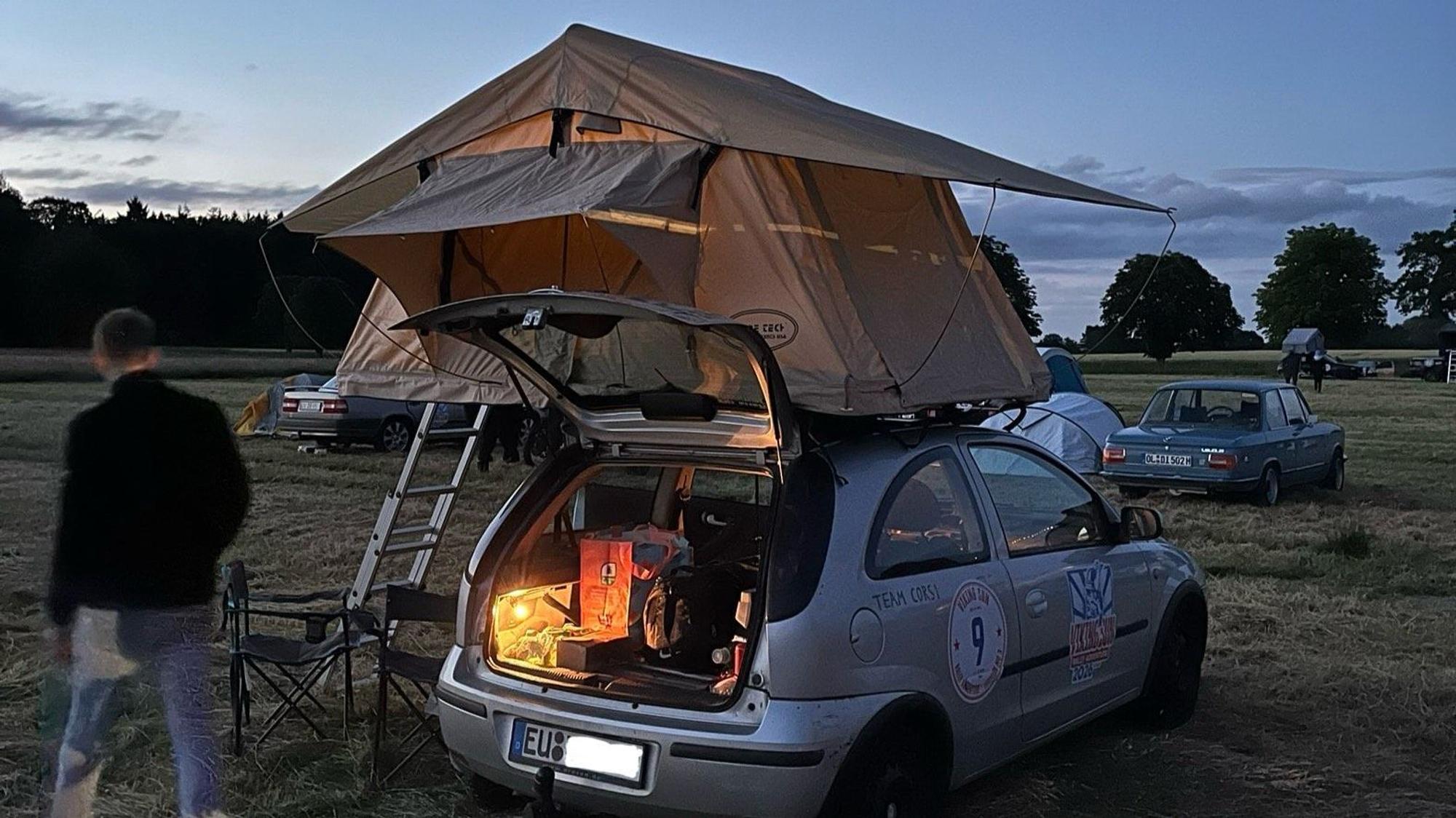 Das Auto steht auf einer Wiese, das Dachzelt mit Leiter ist aufgestellt.