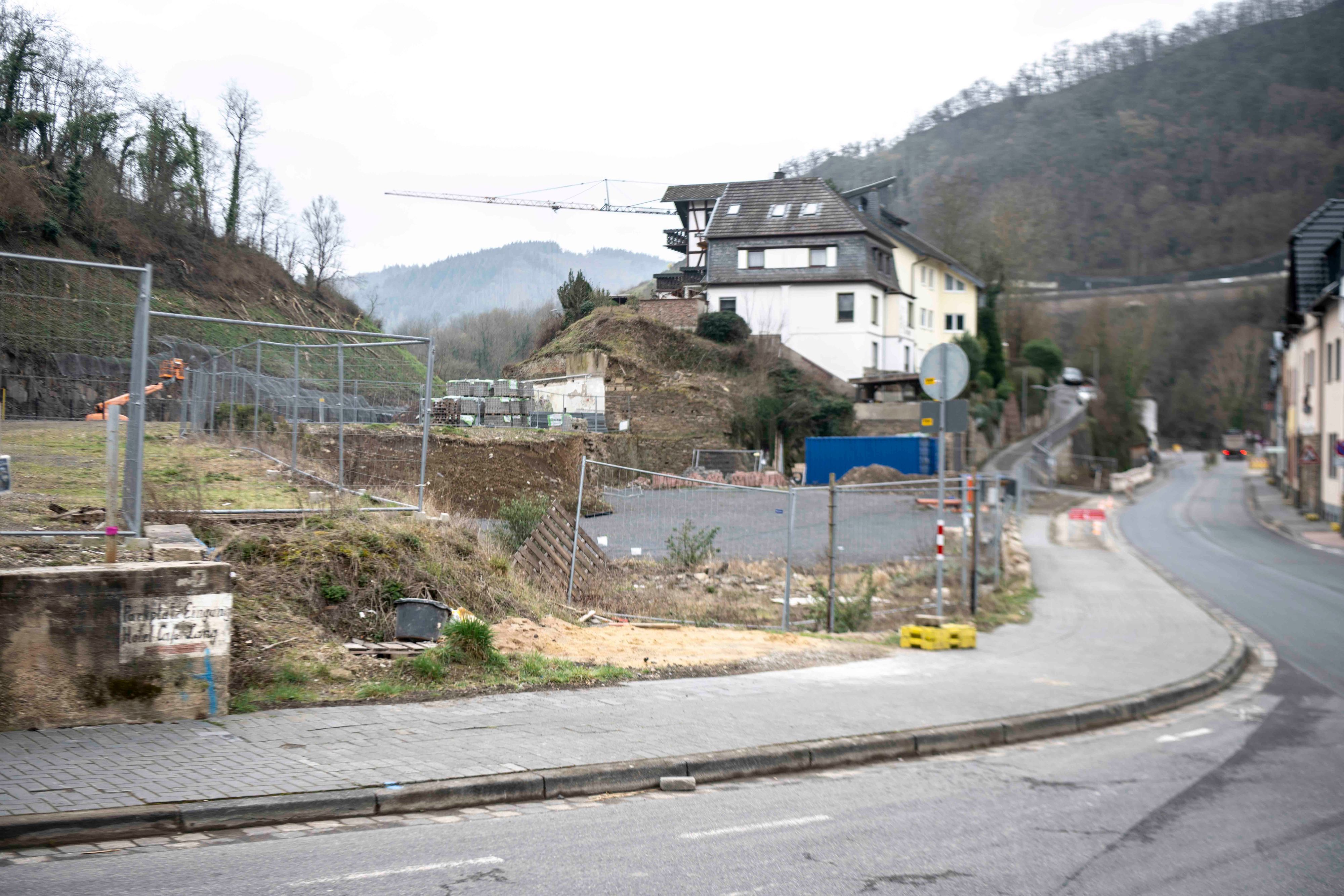 Das Bild zeigt eine Straße im Ahrtal, mit einem leergeräumten Grundstück und einem Kran im Hintergrund.