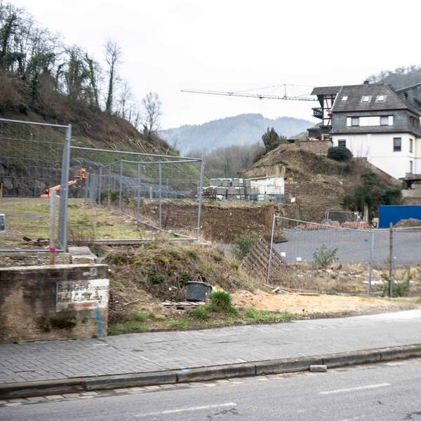 Das Bild zeigt eine Straße im Ahrtal, mit einem leergeräumten Grundstück und einem Kran im Hintergrund.