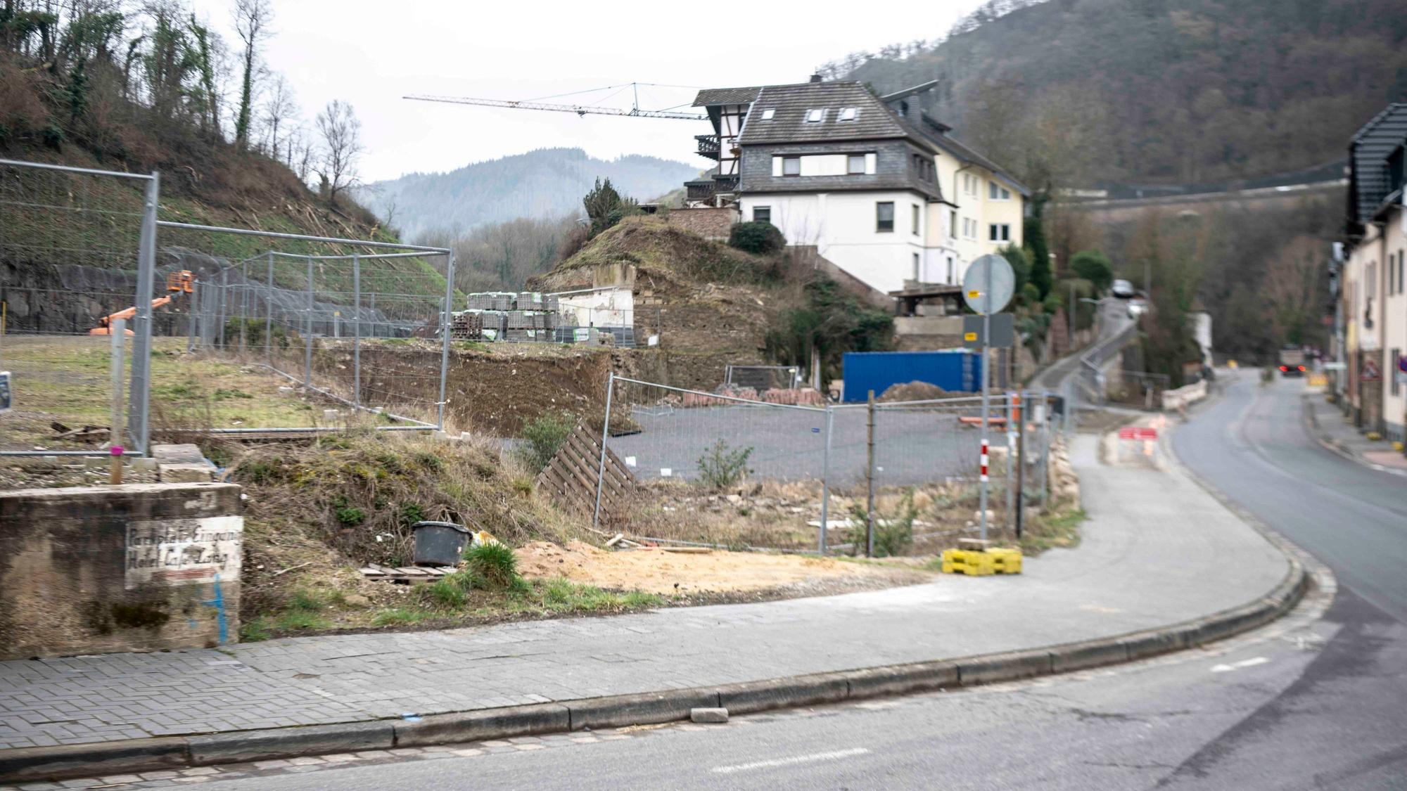Das Bild zeigt eine Straße im Ahrtal, mit einem leergeräumten Grundstück und einem Kran im Hintergrund.
