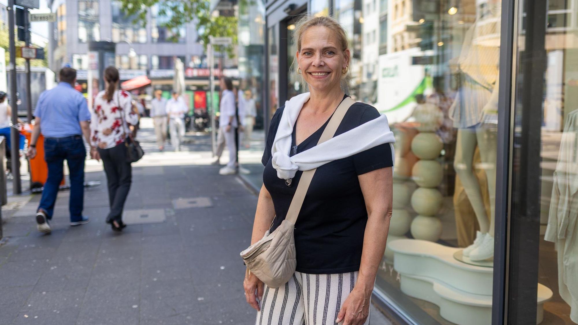 Eine Frau mit Bauchtasche und Pullover um die Schultern lächelt in die Kamera.