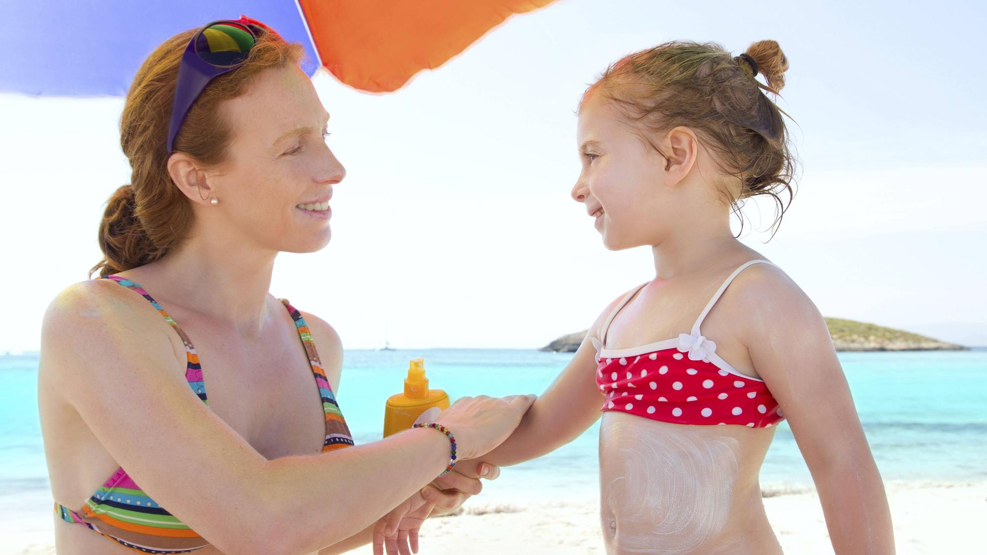 Tochter und Mutter am Strand mit Sonnenschutzmittel.