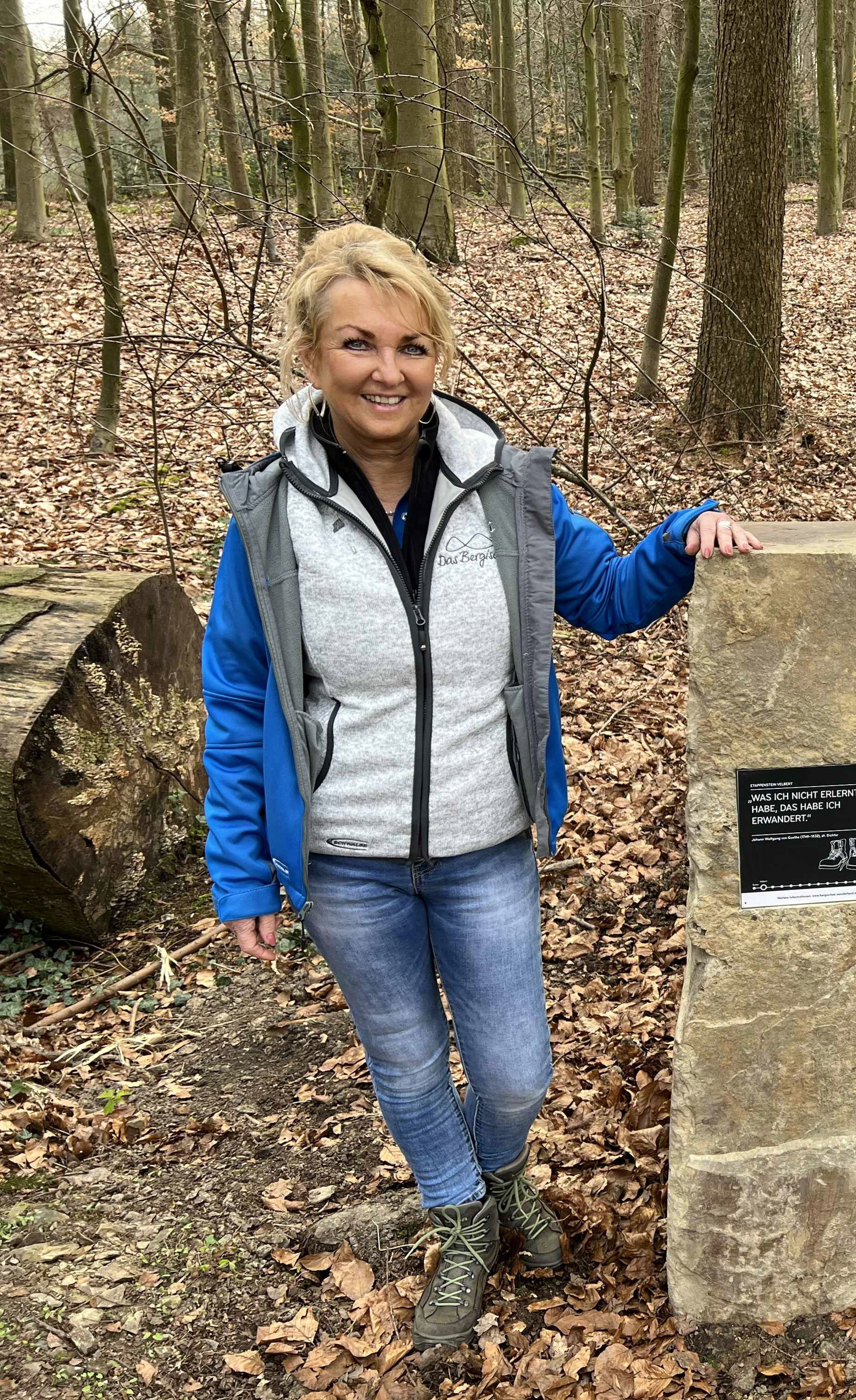 Eine Frau neben einem Findling im Wald.