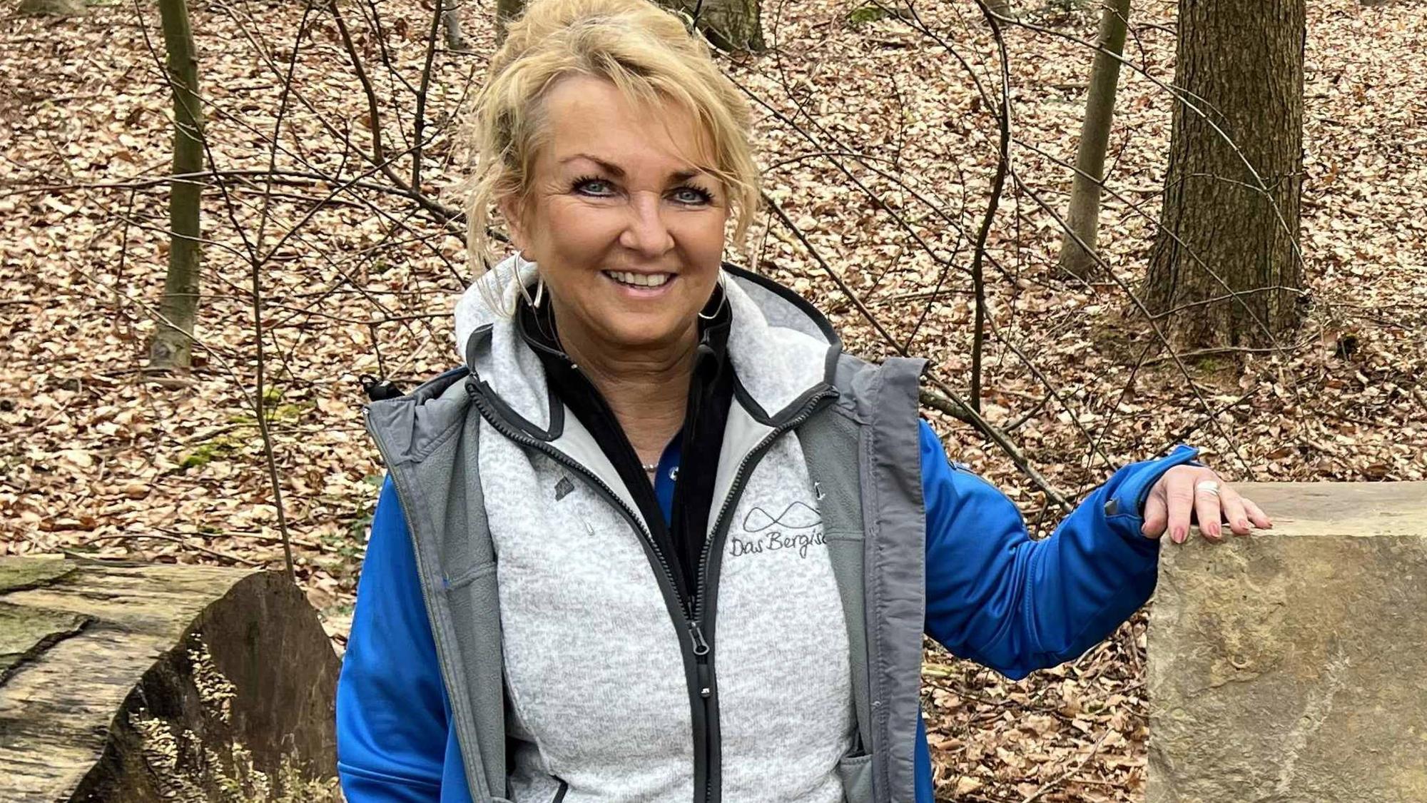 Eine Frau neben einem Findling im Wald.