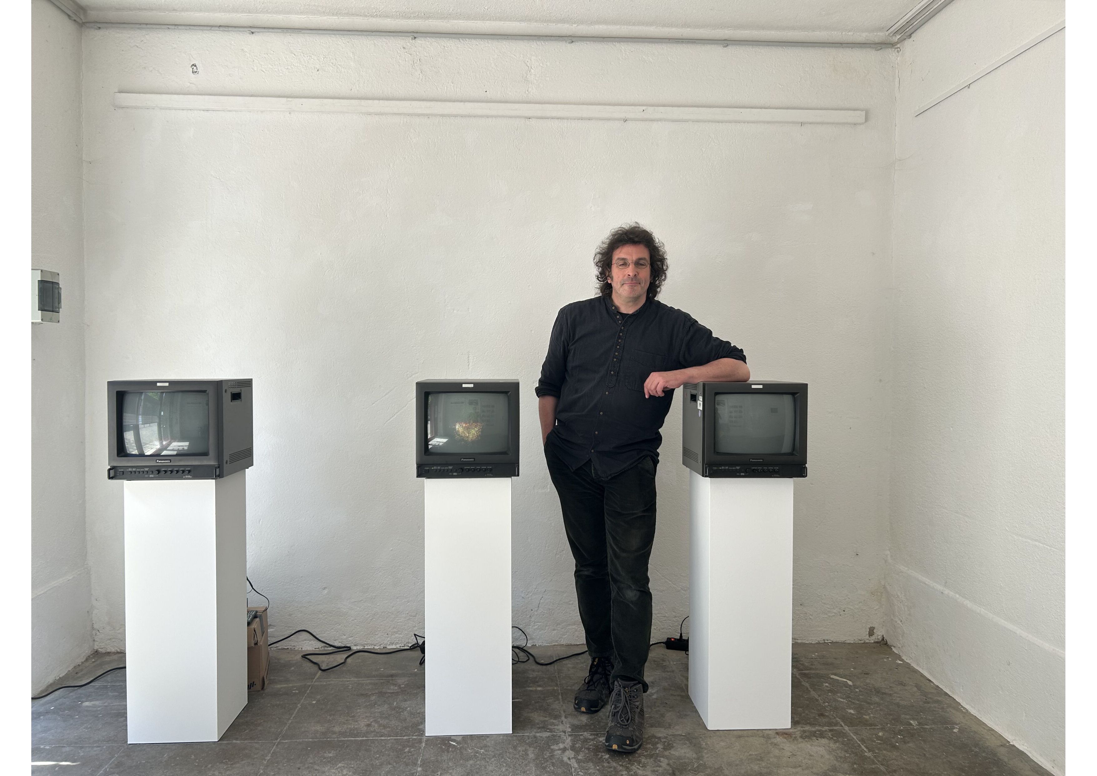Tobias Schmücking vor seiner Videoarbeit mit drei japanischen Winkekatzen, die fragmentarisch auf alten Studiomonitoren zu sehen sind.