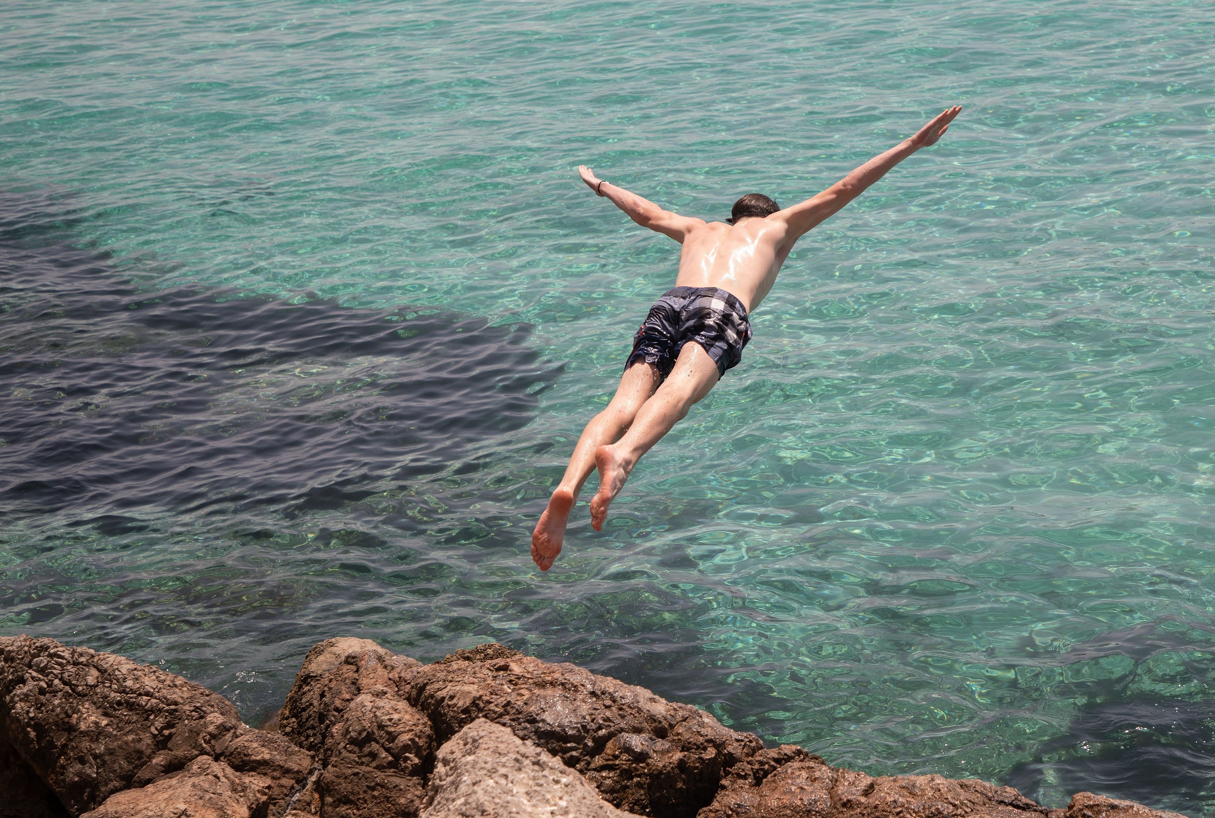 Zu sehen ist ein junger Mann, der in ein Meer springt.