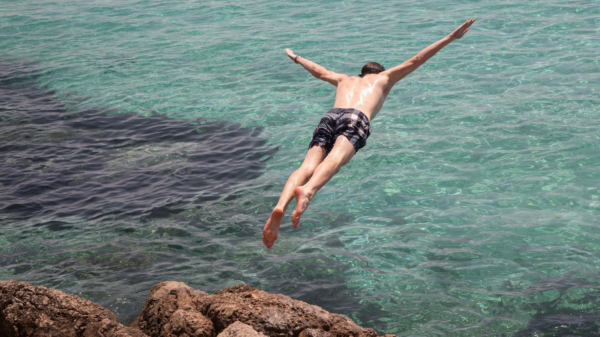 Zu sehen ist ein junger Mann, der in ein Meer springt.