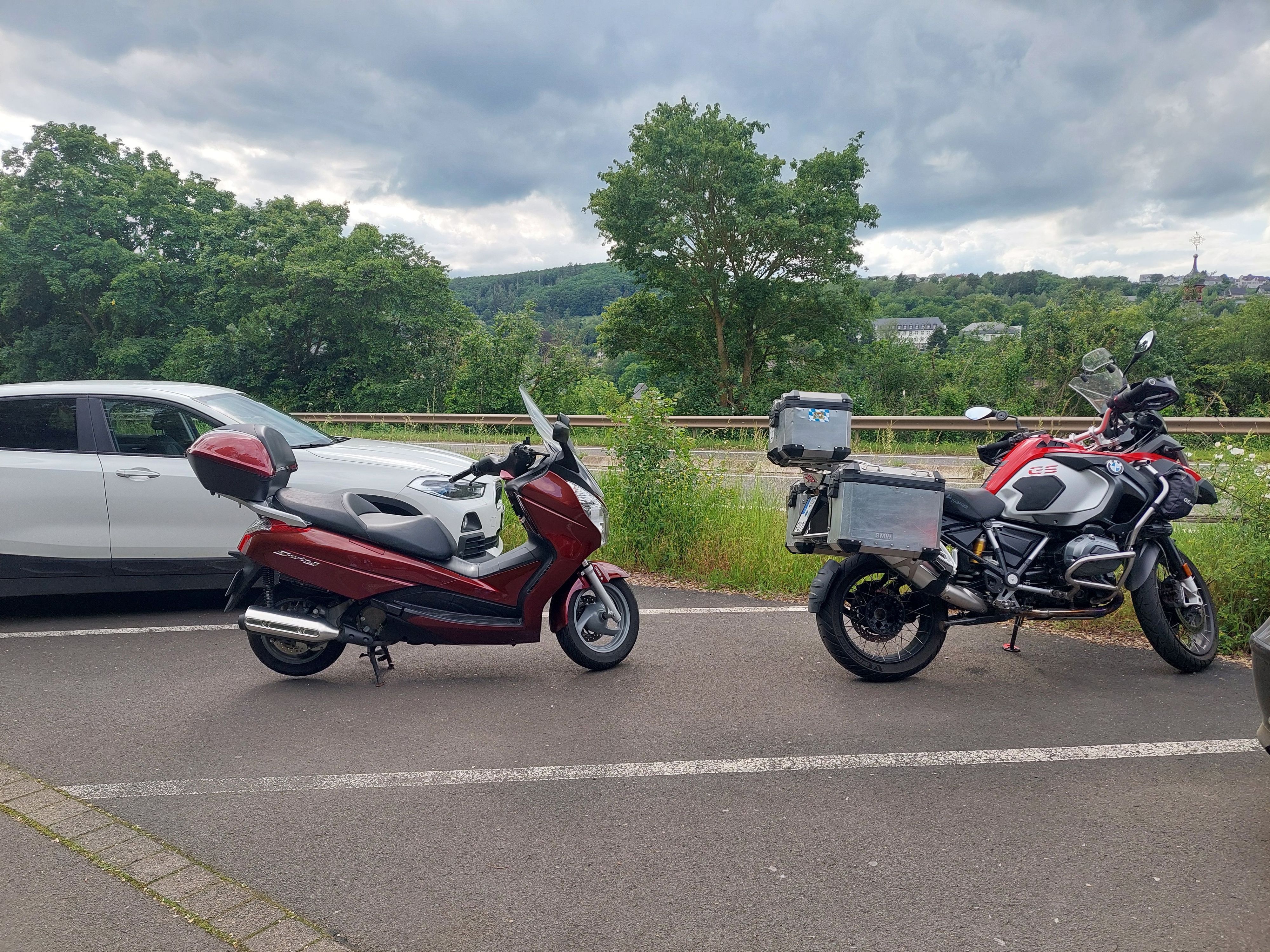 Zwei Motorräder stehen hintereinander in einer Parkbucht.