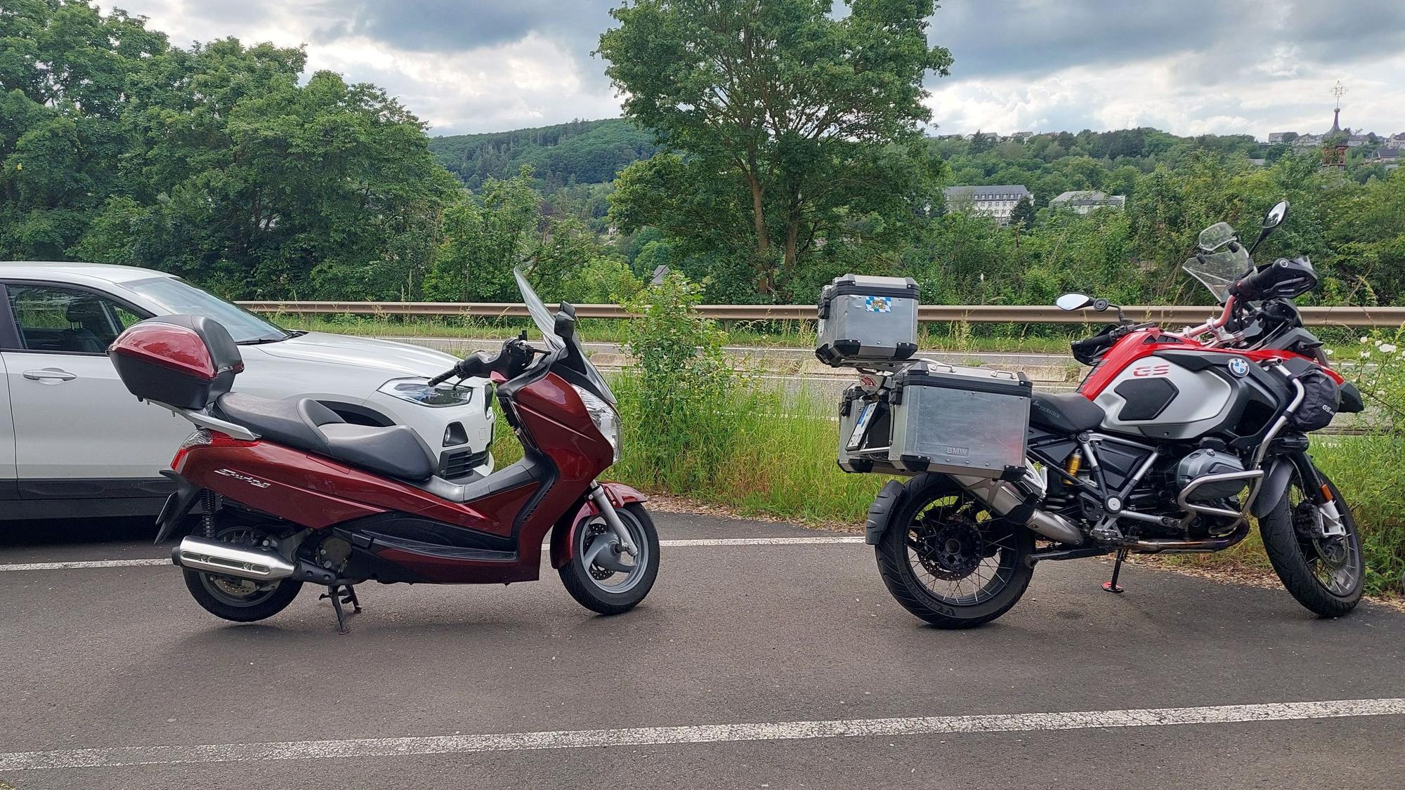 Zwei Motorräder stehen hintereinander in einer Parkbucht.