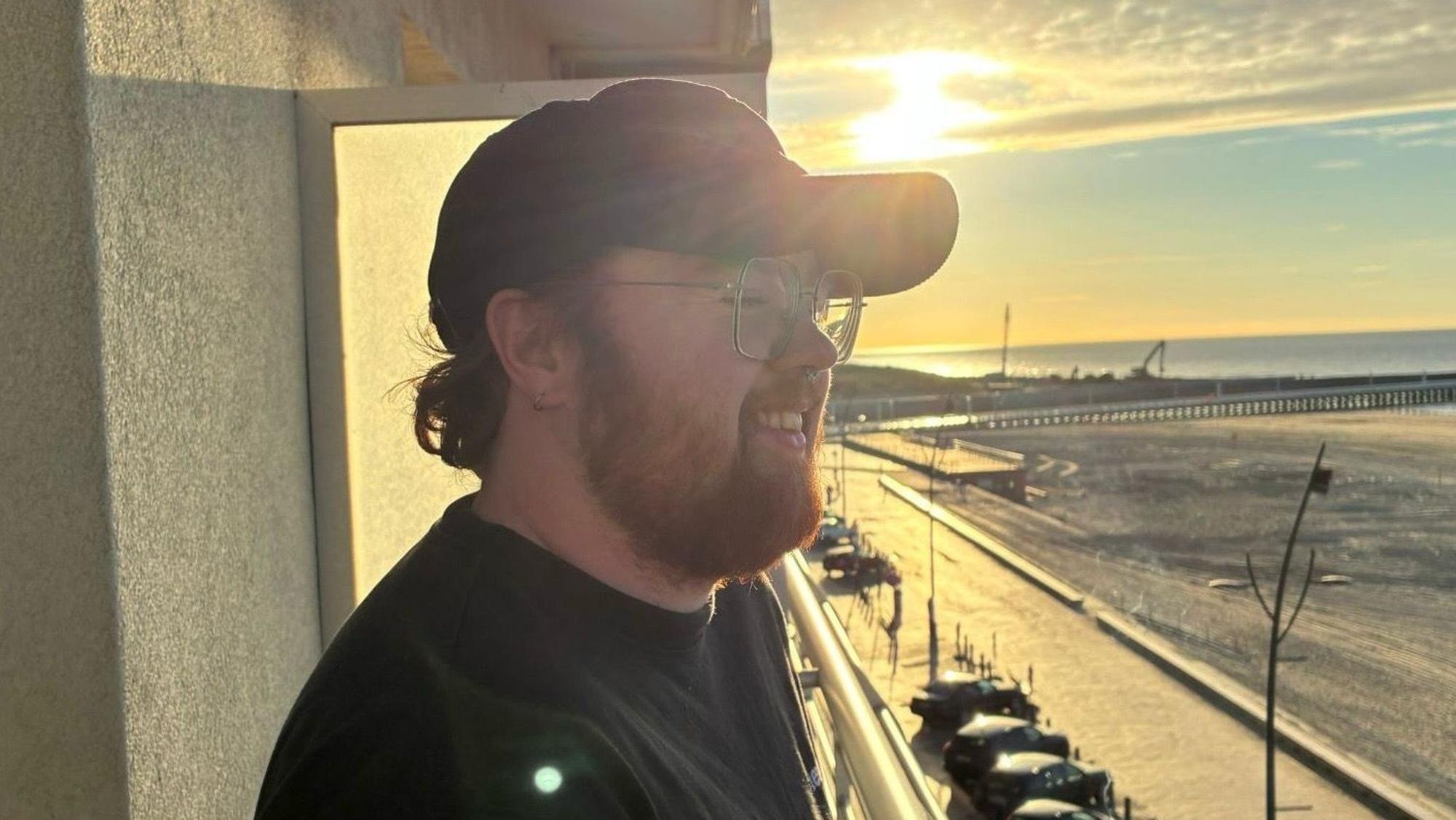 Ein junger Mann steht draußen, im Hintergrund geht die Sonne unter