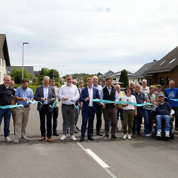 Eine Gruppe Menschen steht auf der Straße. Sie durchschneiden an meheren Stellen ein blaues Band.
