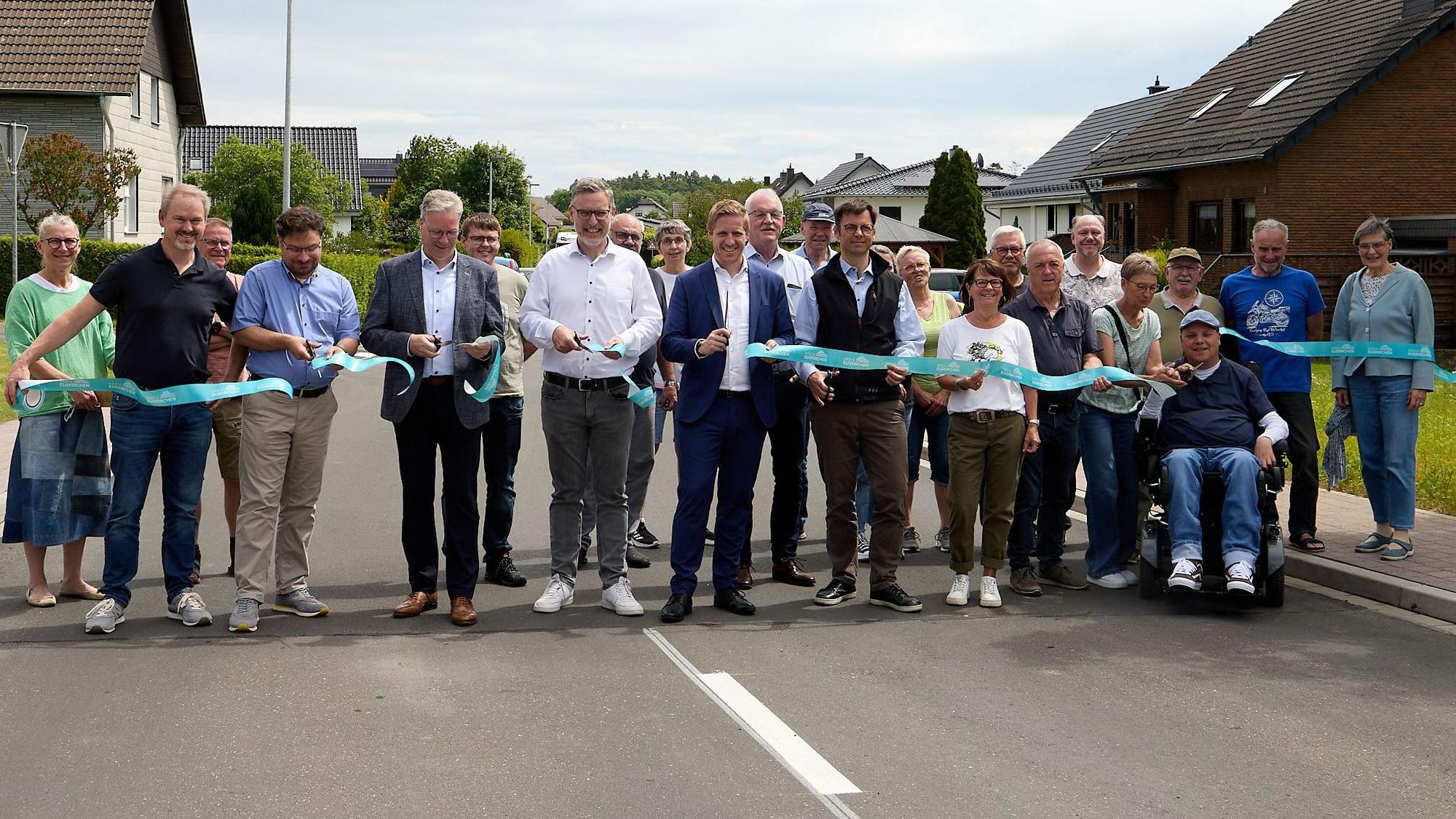 Eine Gruppe Menschen steht auf der Straße. Sie durchschneiden an meheren Stellen ein blaues Band.