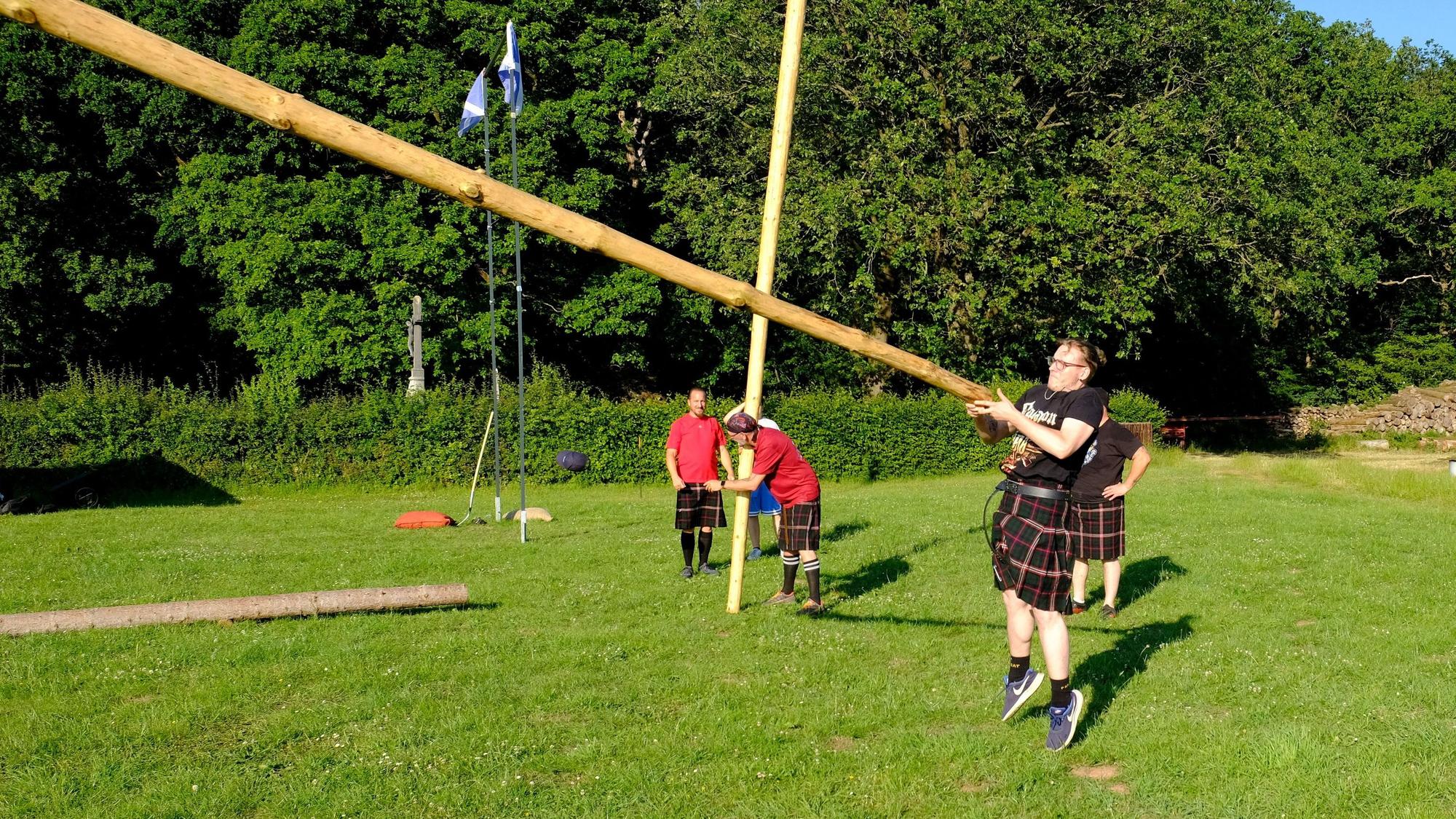 Ein Athlet der Hunting Tartans im Kilt beim Baumstammwerfen auf dem Bolzplatz in Hostel.