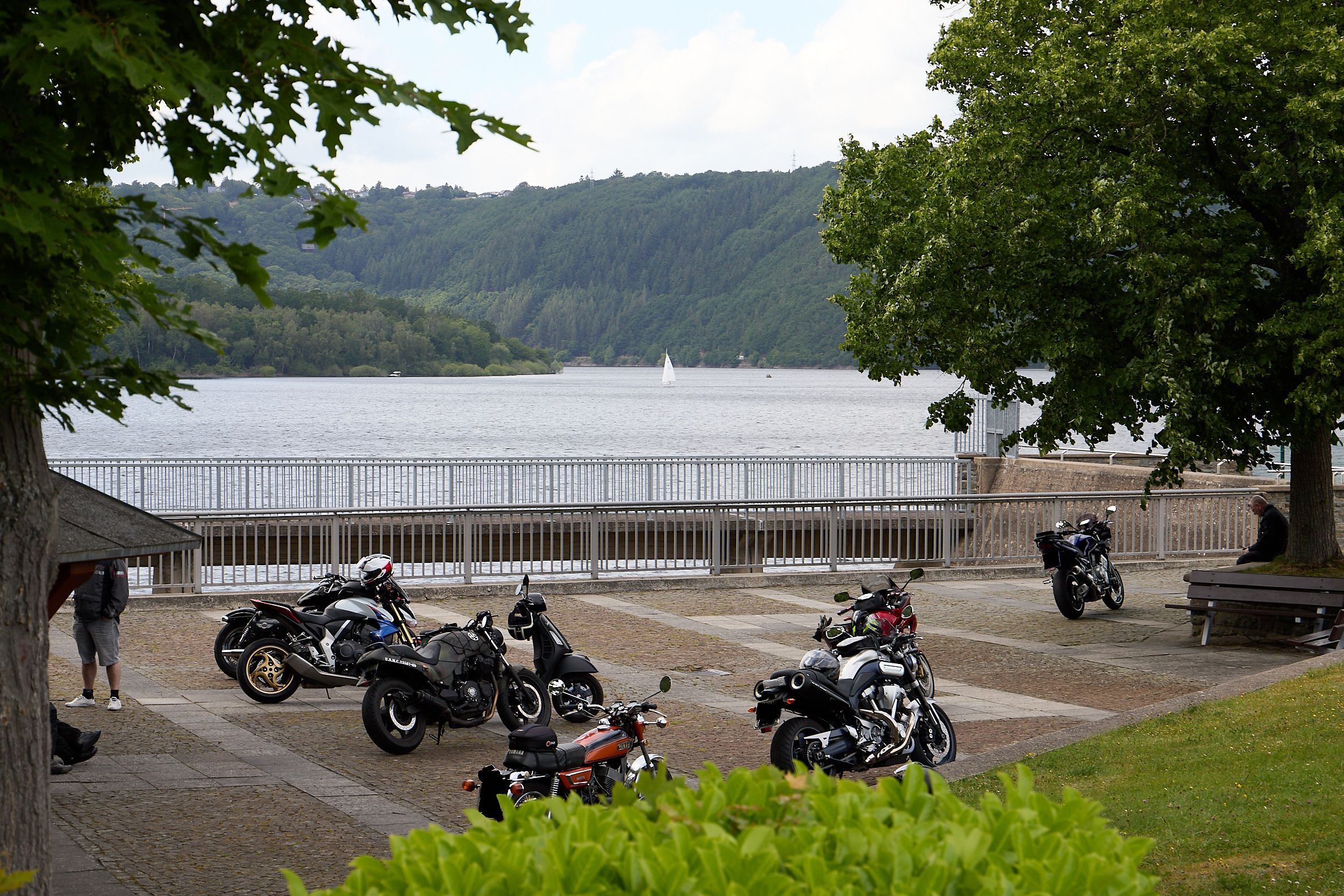 Neun Motorräder stehen auf einer Fläche in Schwammenauel. Im Hintergrund ist die Talsperre zu sehen.