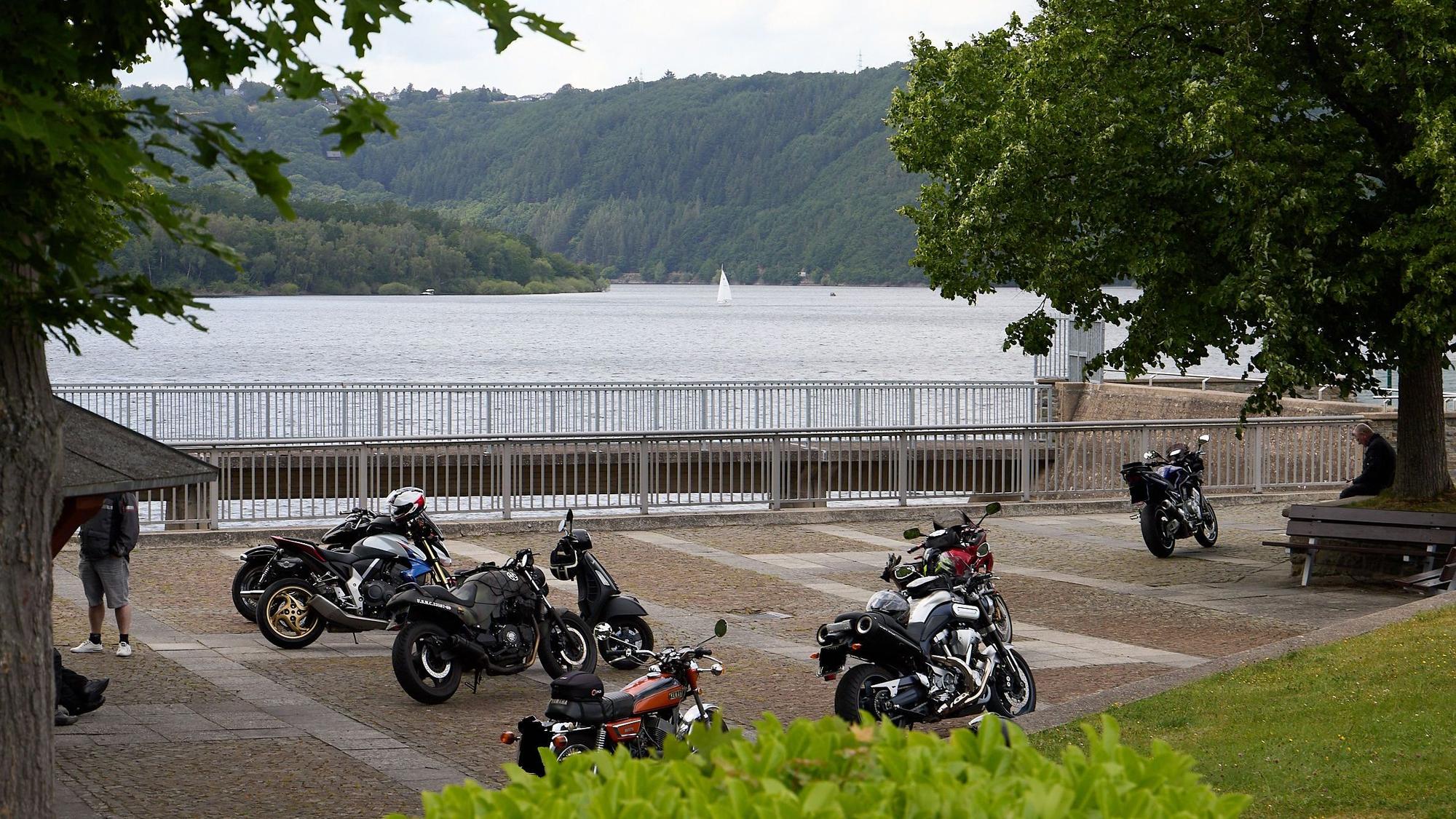 Neun Motorräder stehen auf einer Fläche in Schwammenauel. Im Hintergrund ist die Talsperre zu sehen.