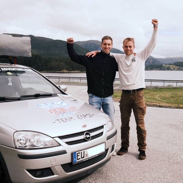 Die Zülpicher Henrik Krewel (l.) und Andreas Ulm stehen neben ihrem Opel Corsa und recken jubelnd je einen Arm in die Höhe. Im Hintergrund ist ein See zu sehen.