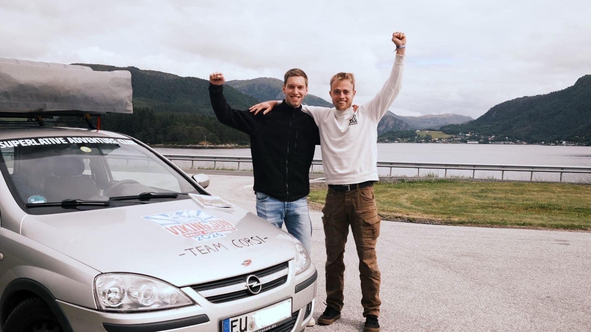 Die Zülpicher Henrik Krewel (l.) und Andreas Ulm stehen neben ihrem Opel Corsa und recken jubelnd je einen Arm in die Höhe. Im Hintergrund ist ein See zu sehen.