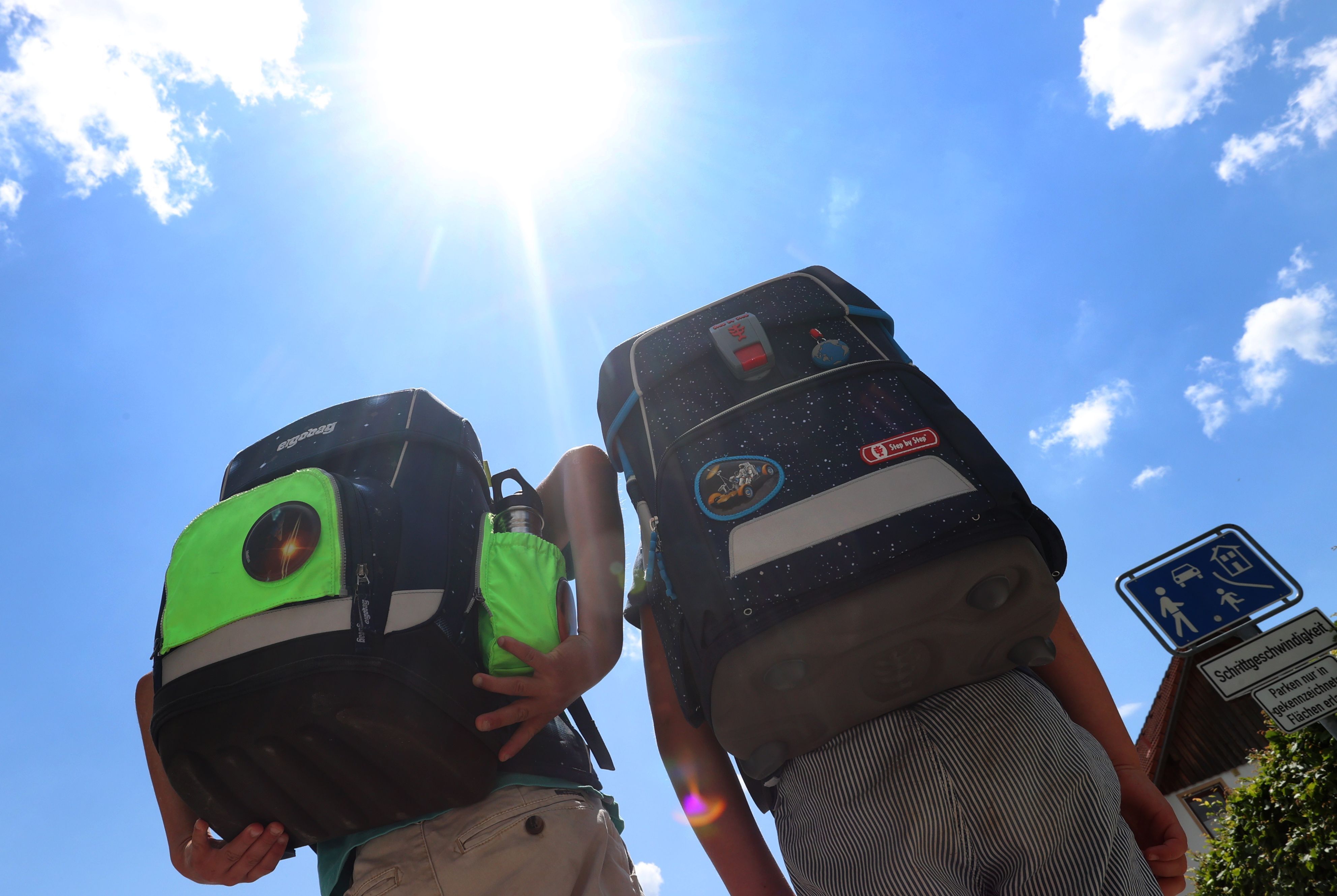 Zwei Kinder laufen mit ihren Büchertaschen im Sonnenschein. Sehr hohe Temperaturen führen an Schulen zu Hitzefrei – aber das ist keine Dauerlösung. (Symbolbild)