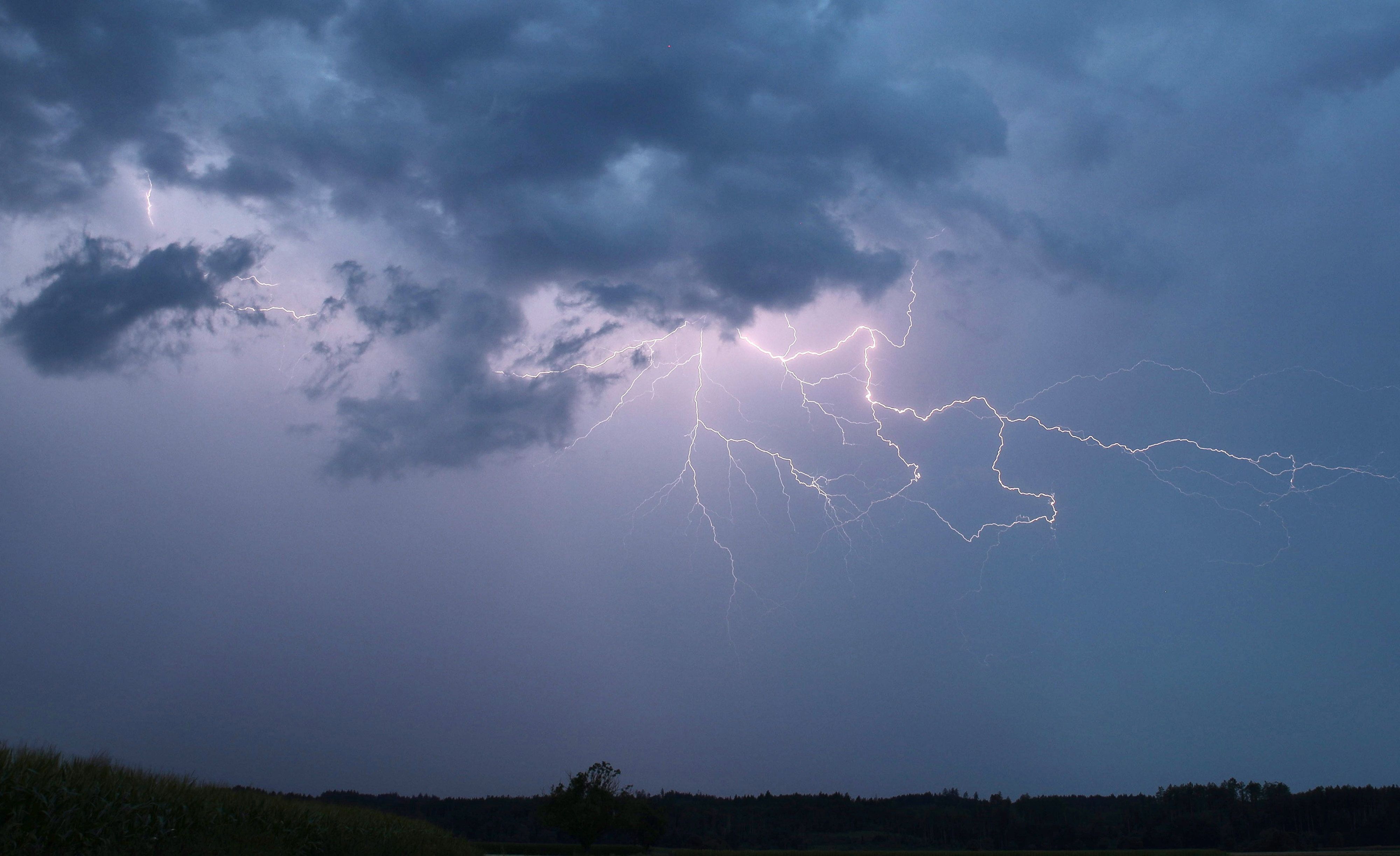 Ein Blitz zuckt bei einem Sommergewitter am abendlichen Himmel.