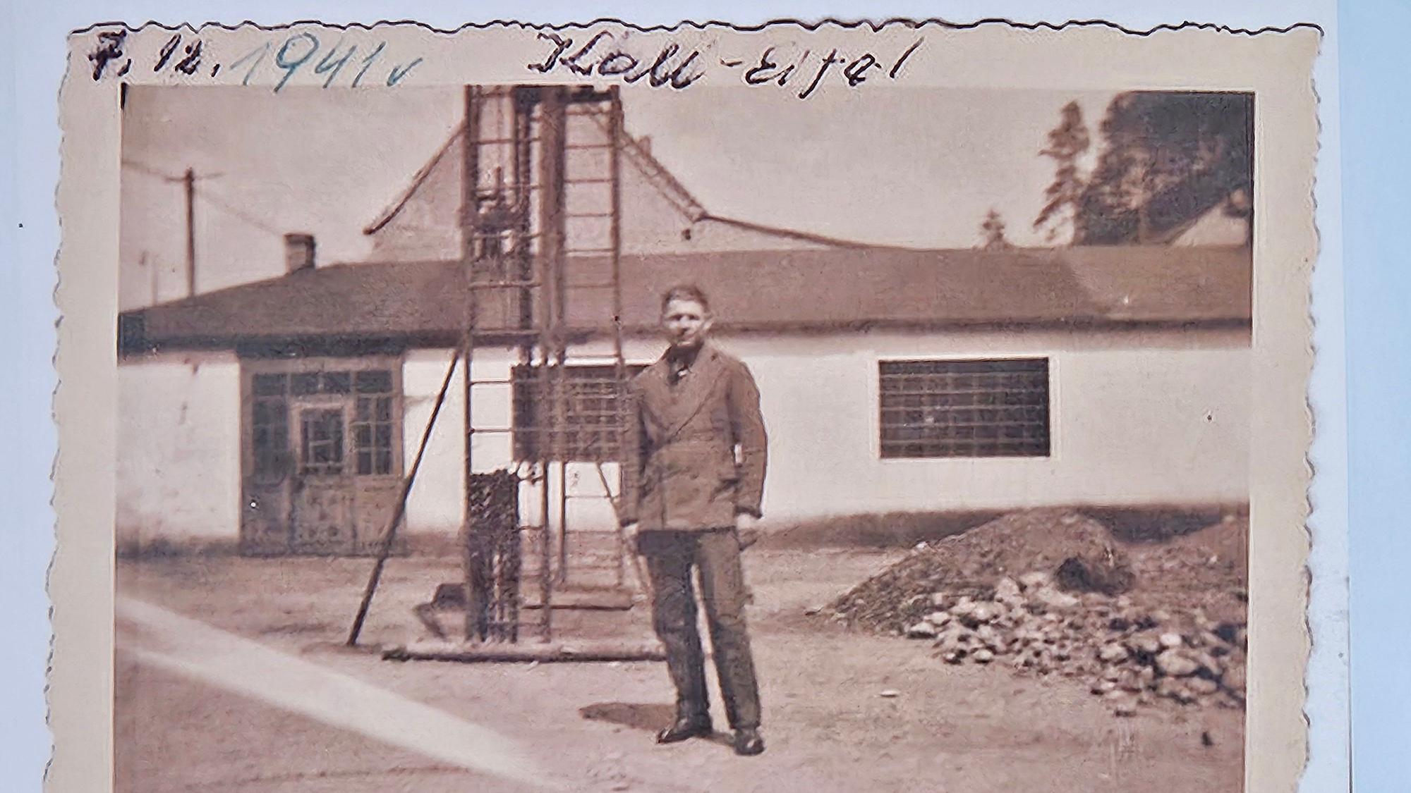 Das Bild ist ein schwarz-weiß Foto. Ein Mann steht vor einer Halle.