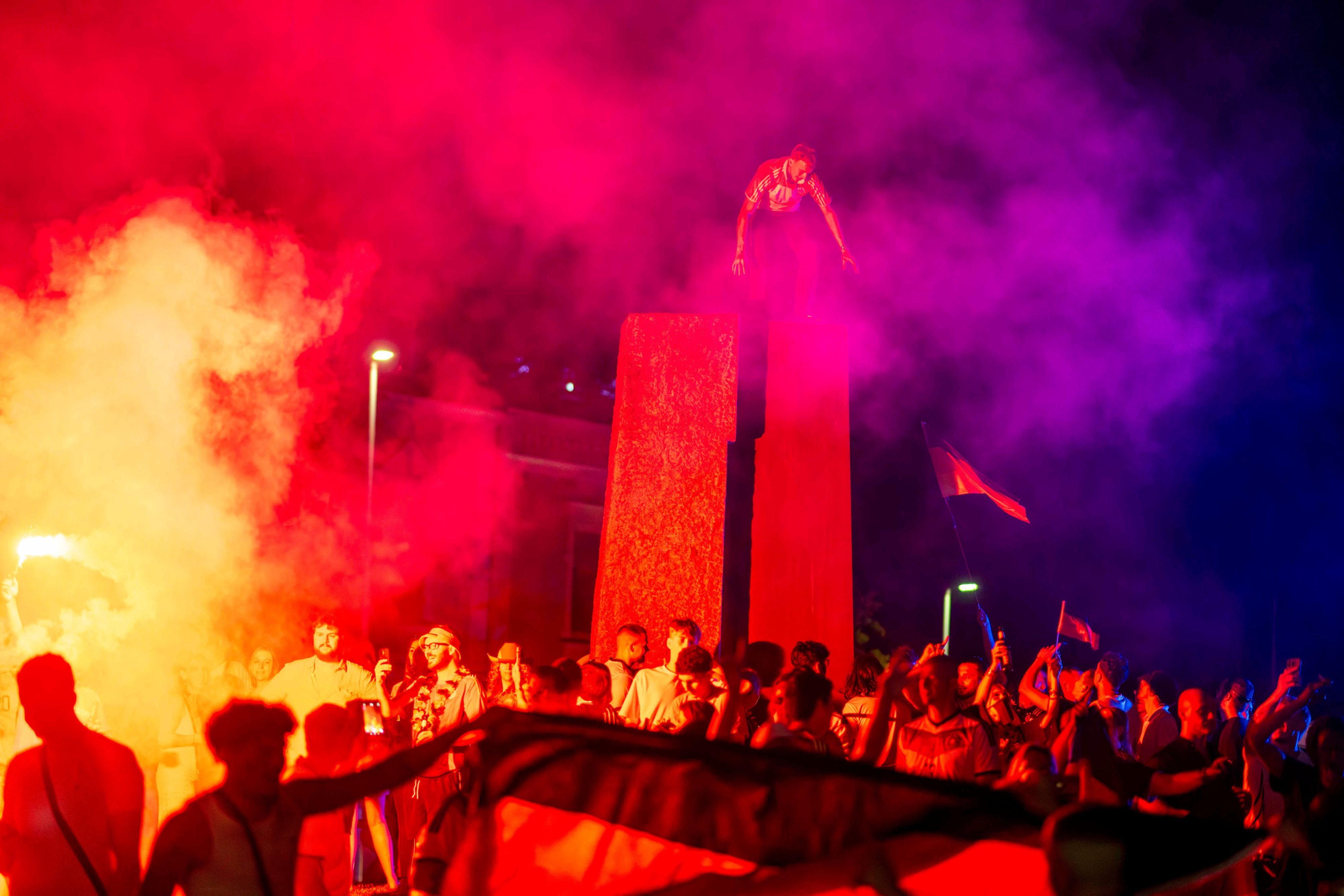 Fußballfans feiern im Schein der bengalischen  Lichter. Ein Mann ist auf die Stele im Kreisverkehr geklettert.
