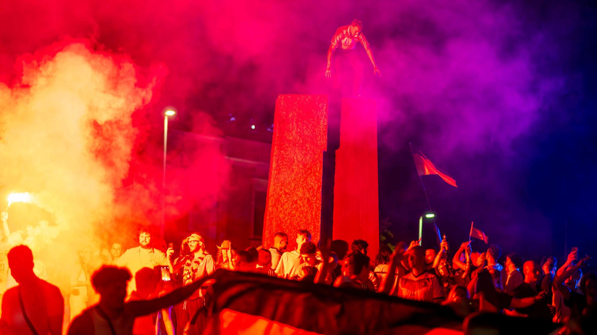 Fußballfans feiern im Schein der bengalischen Lichter. Ein Mann ist auf die Stele im Kreisverkehr geklettert.