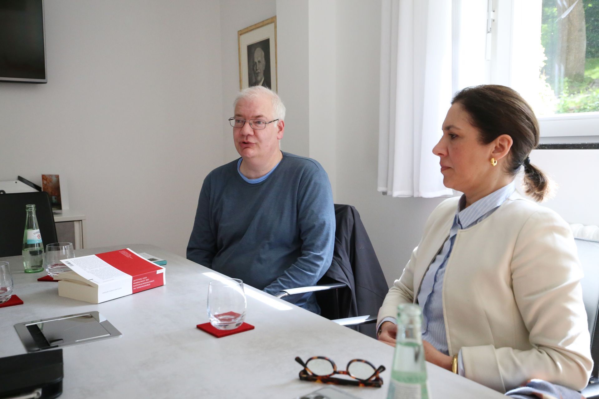 Die Obengenannten sitzen an einem Tisch und schauen in unterschiedliche Richtungen auf etwas außerhalb des Bildausschnitts.