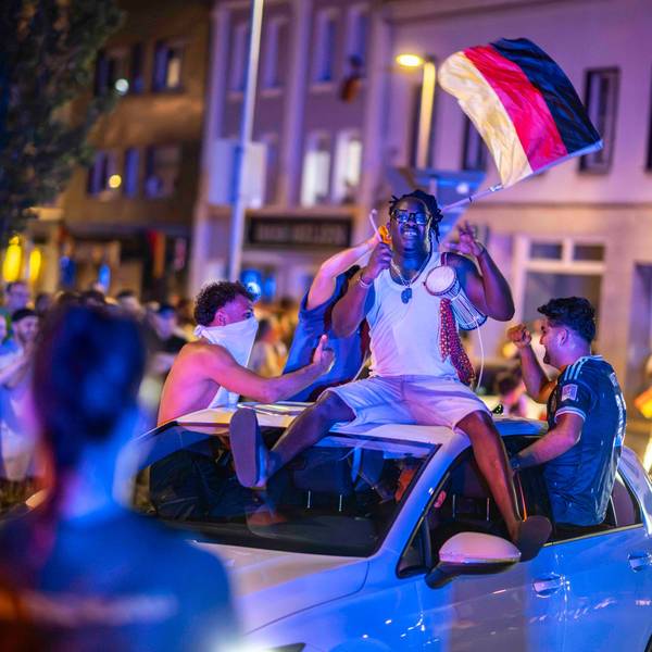 Autos drehen ihre Runde durch den Kreis-Verkehr. Auf dem Dach eines Wagens sitzt ein Mann mit einer kleinen Trommel. Ein anderer wedelt mit den Deutschland-Fahne.