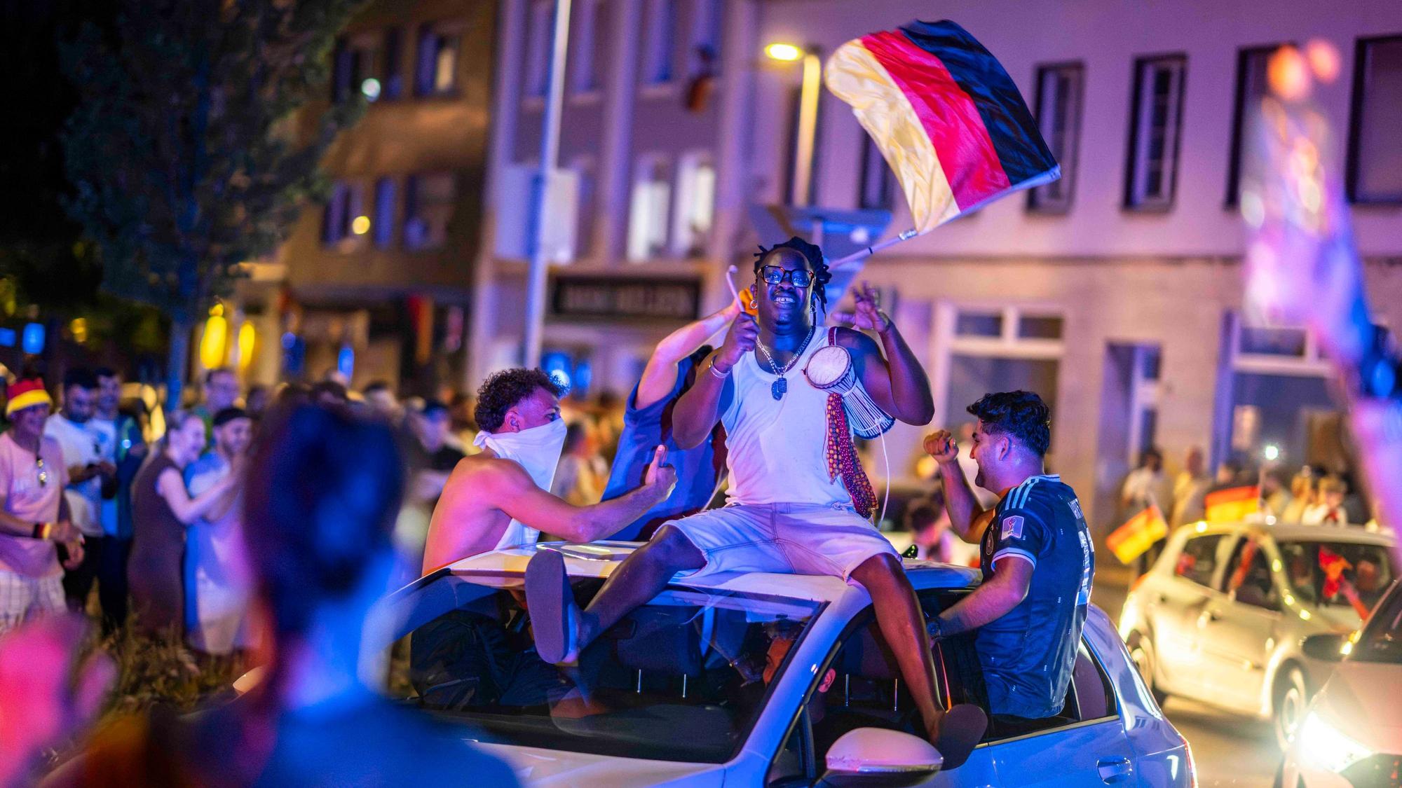 Autos drehen ihre Runde durch den Kreis-Verkehr. Auf dem Dach eines Wagens sitzt ein Mann mit einer kleinen Trommel. Ein anderer wedelt mit den Deutschland-Fahne.