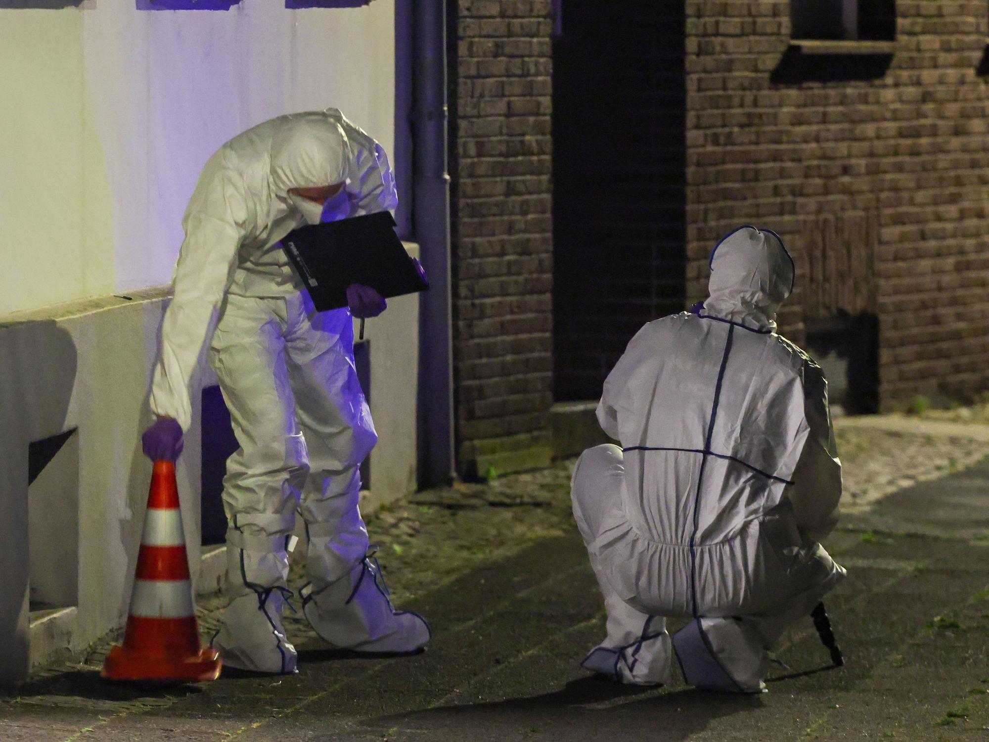 Zwei Beamte der Spurensicherung in Spurensicherungsanzügen begutachten den Tatort vor einem Mehrfamilienhaus im Stadtteil Uerdingen.