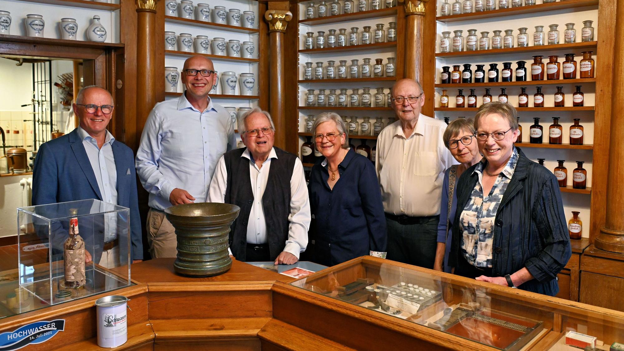 Die genannten Personen stehen im historischen Apothekengebäude vor Regalen mit zahlreichen Flaschen und anderen Behältnissen.