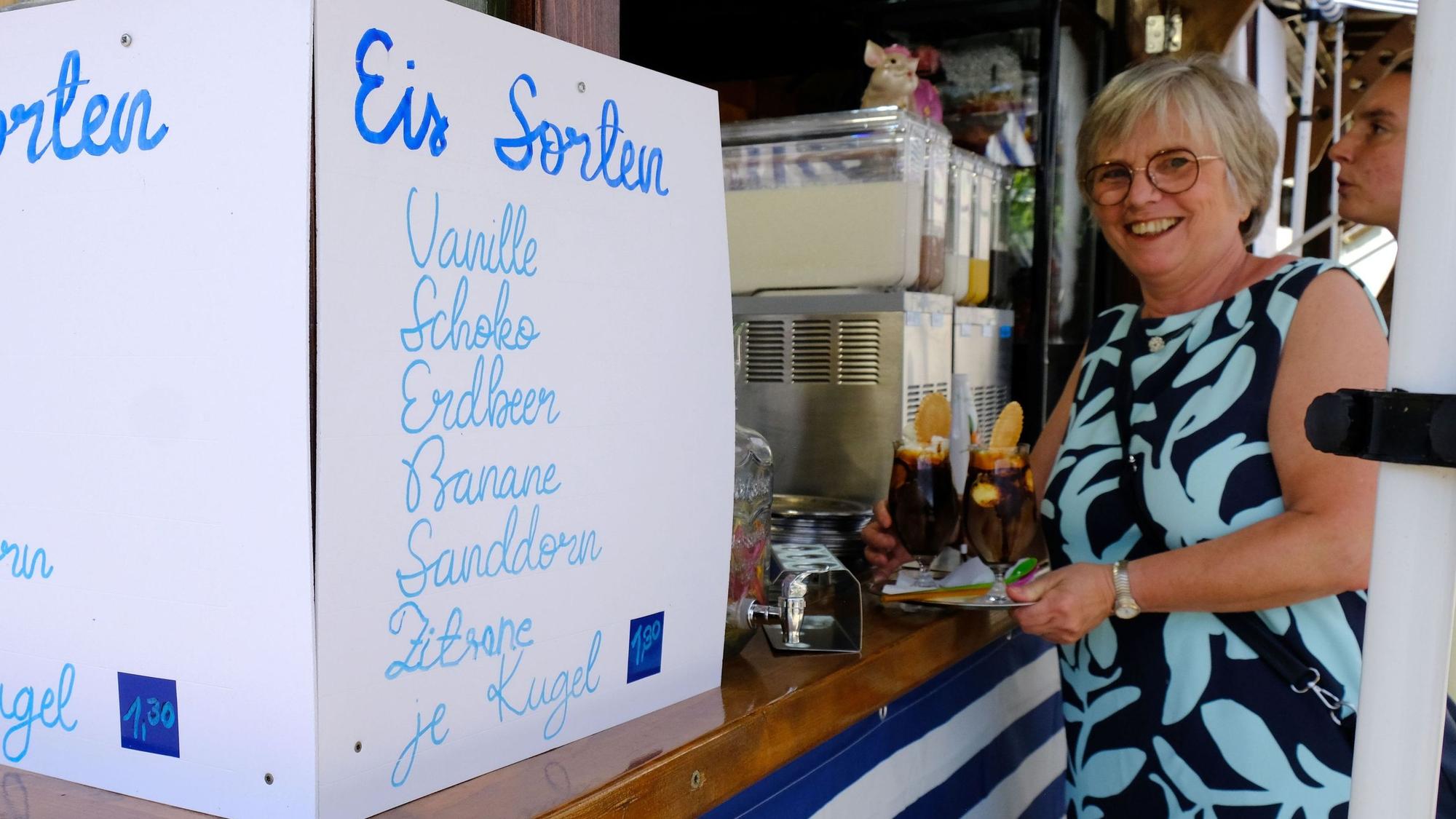 Neben einem Schild, auf dem die Sorten aufgeführt sind, steht eine Frau mit zwei Getränken auf einem Tablett.