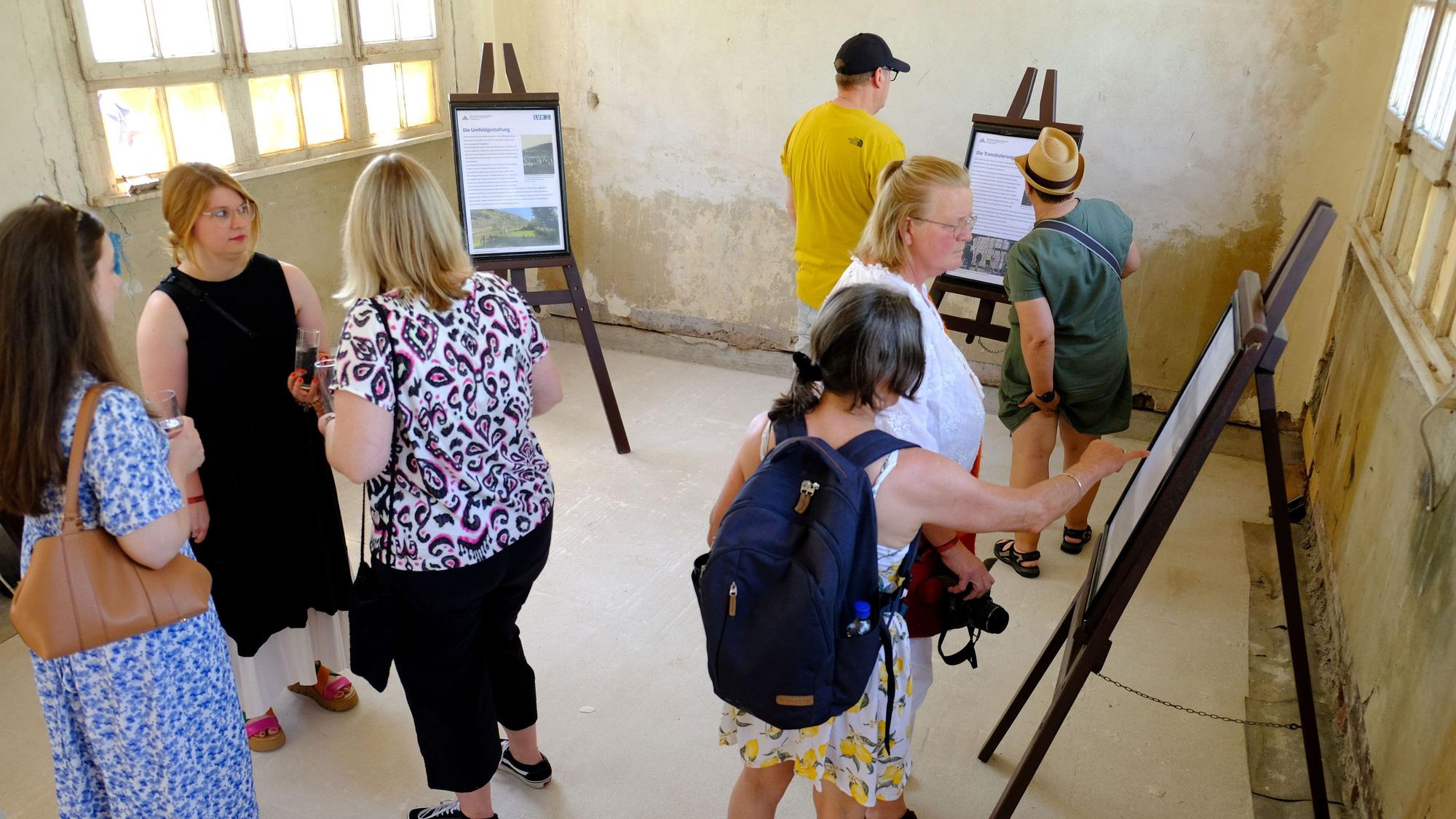 Mehrere Besucher halten sich im Wartesaal des Bahnhofs auf, der sich noch im Rohzustand befindet und in dem mehrere Infotafeln aufgebaut sind.