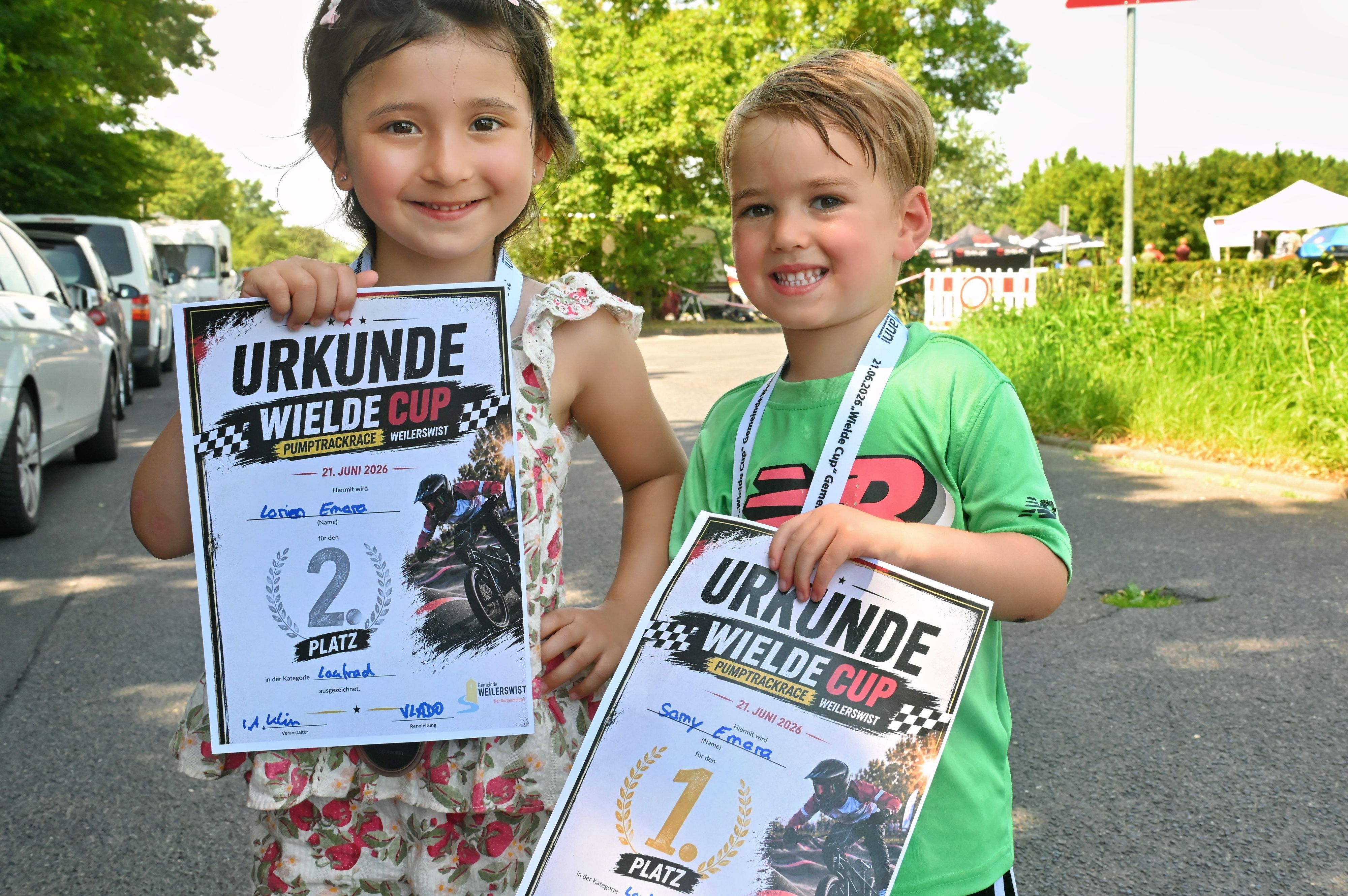 Ein Mädchen und ein Junge zeigen ihre Urkunen und strahlen.