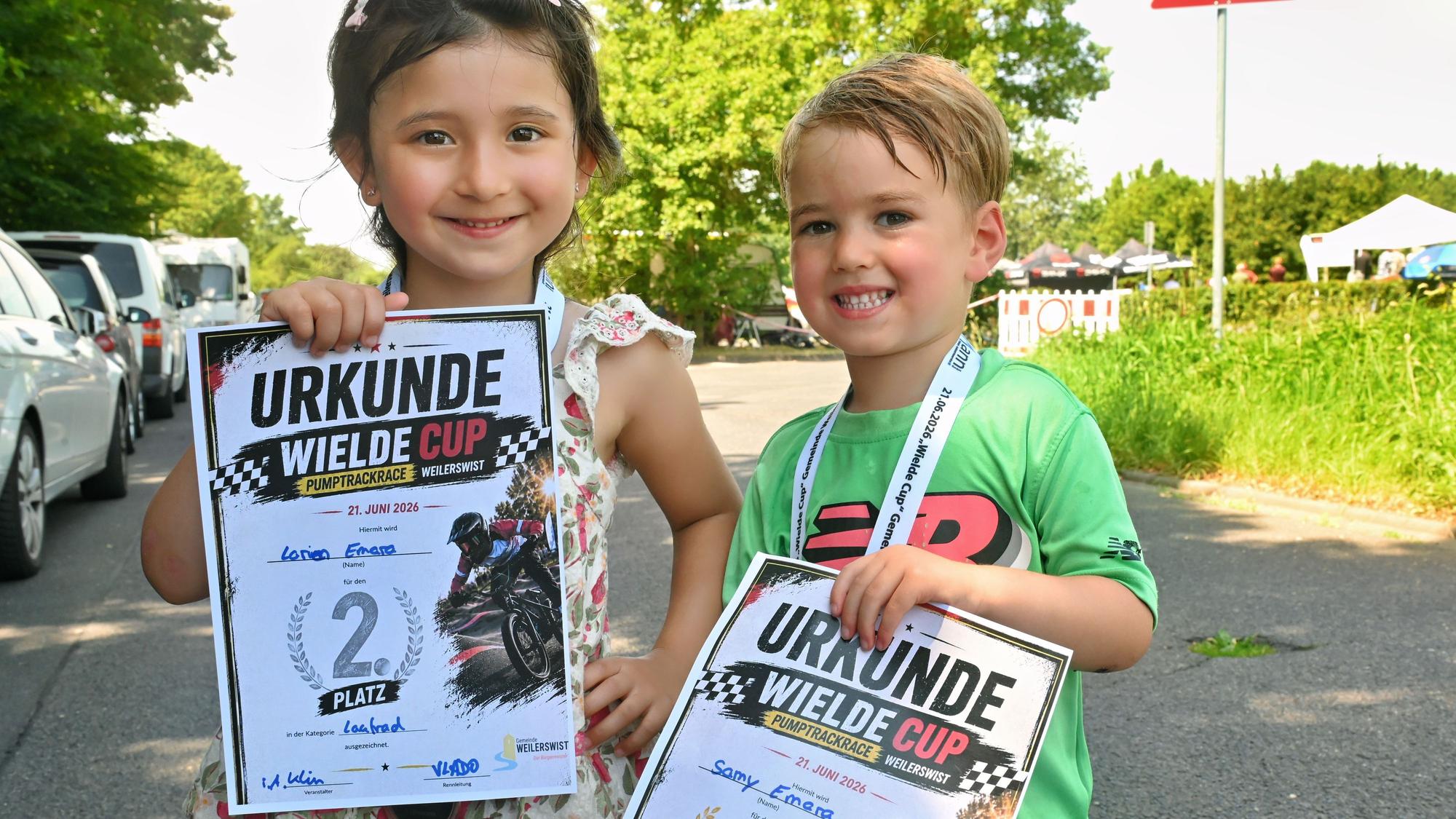 Ein Mädchen und ein Junge zeigen ihre Urkunen und strahlen.