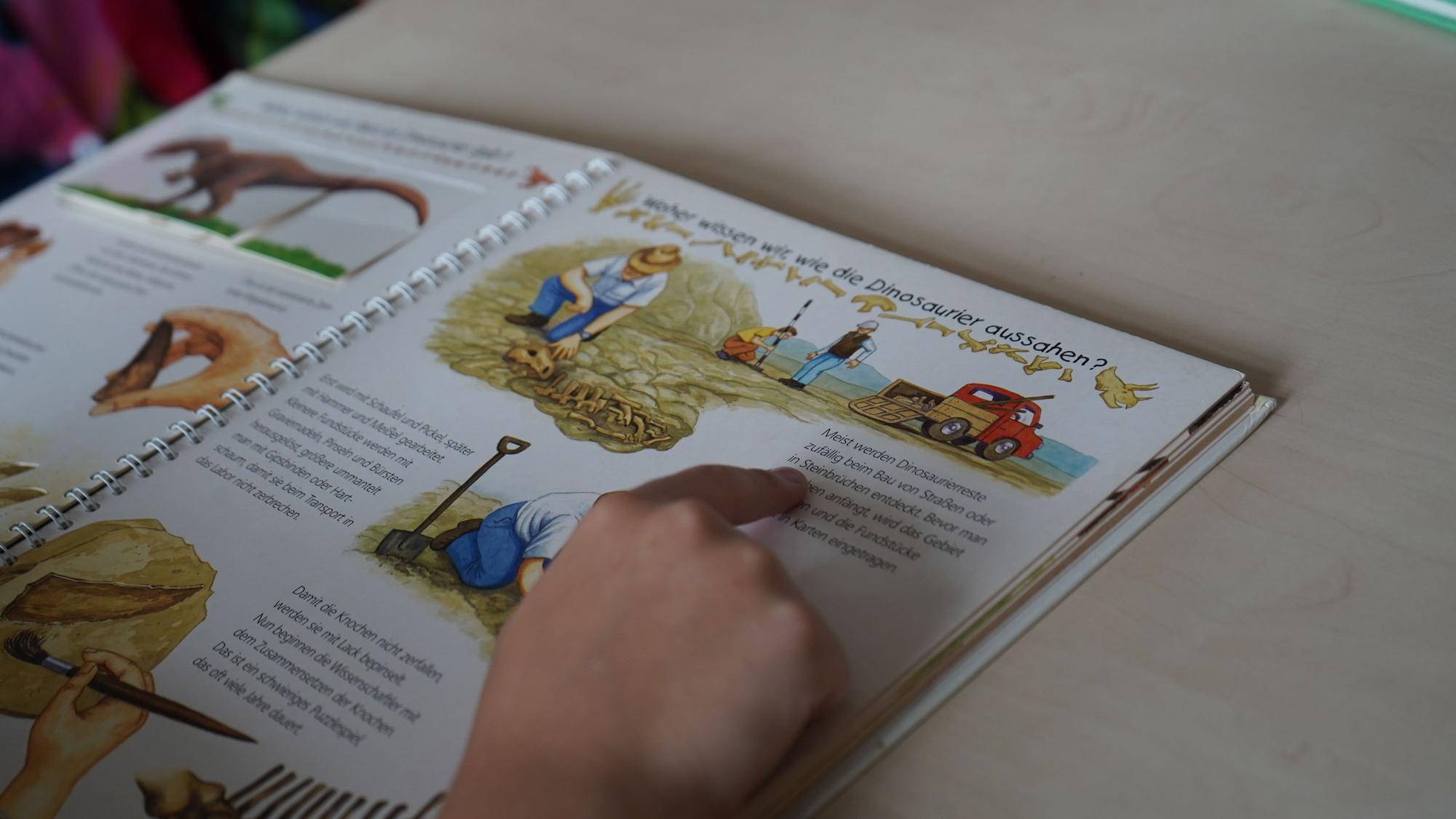 Das Bild zeigt die Hand eines Kindes am Buch. Mit dem Zeigefinger fährt es die Zeilen des Texts entlang.