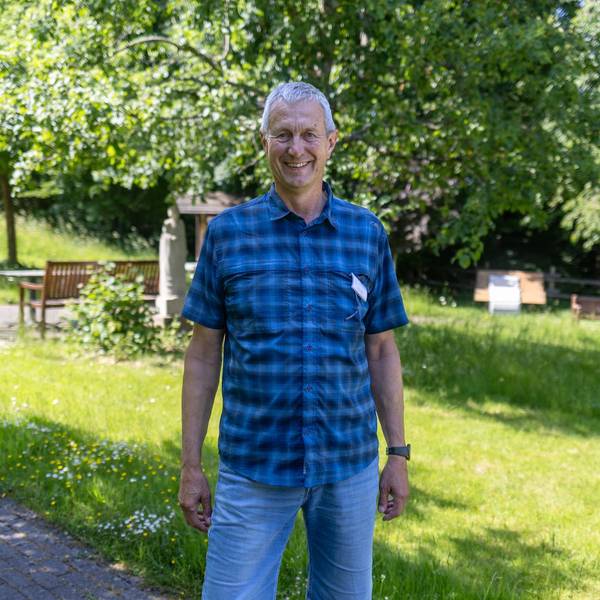 Ein Mann im karierten Hemd steht in einem Garten.