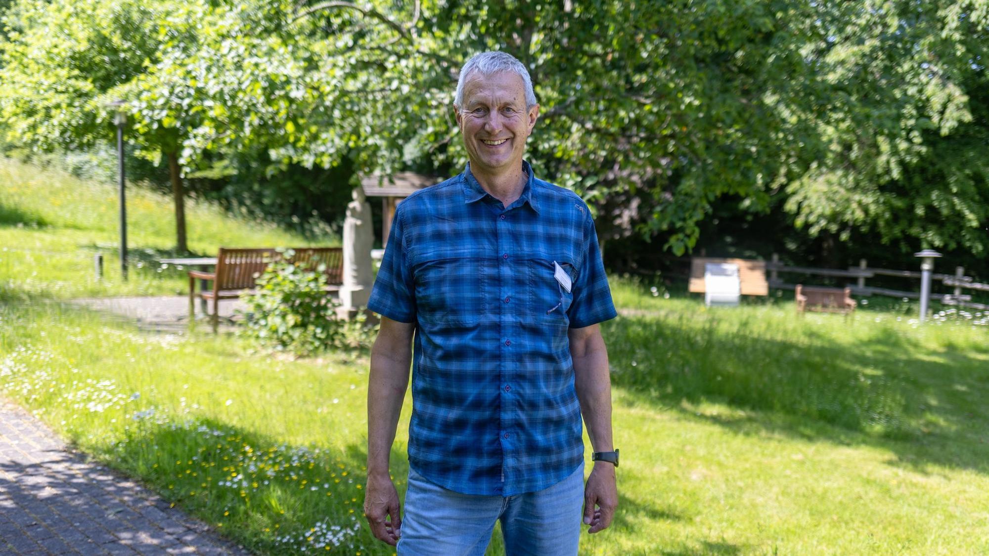 Ein Mann im karierten Hemd steht in einem Garten.