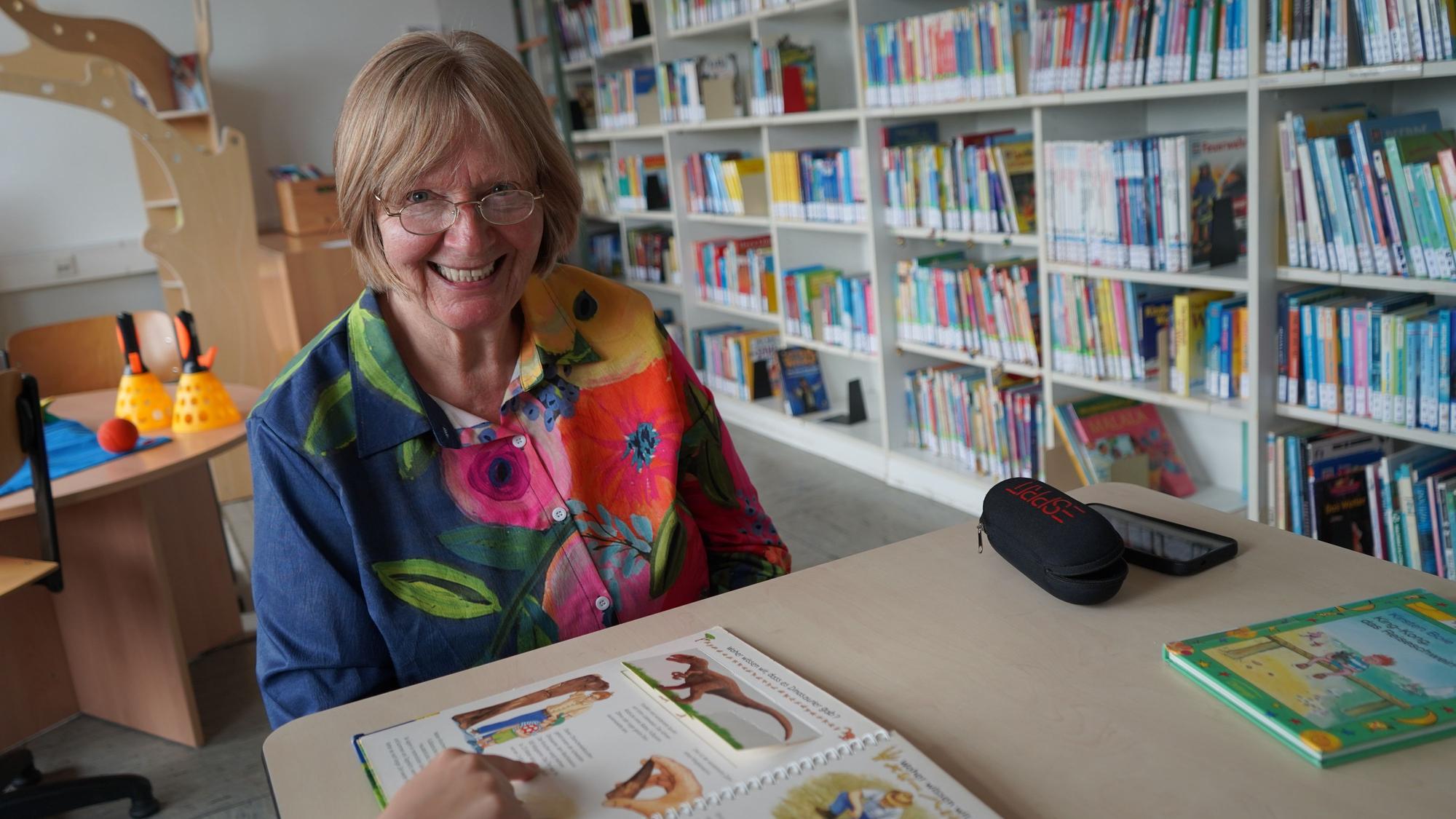 Das Bild zeigt die Seniorin im Lesewald der Rochusschule in Glessen. Vor ihr zeigt ein Kind gerade auf ein Buch.
