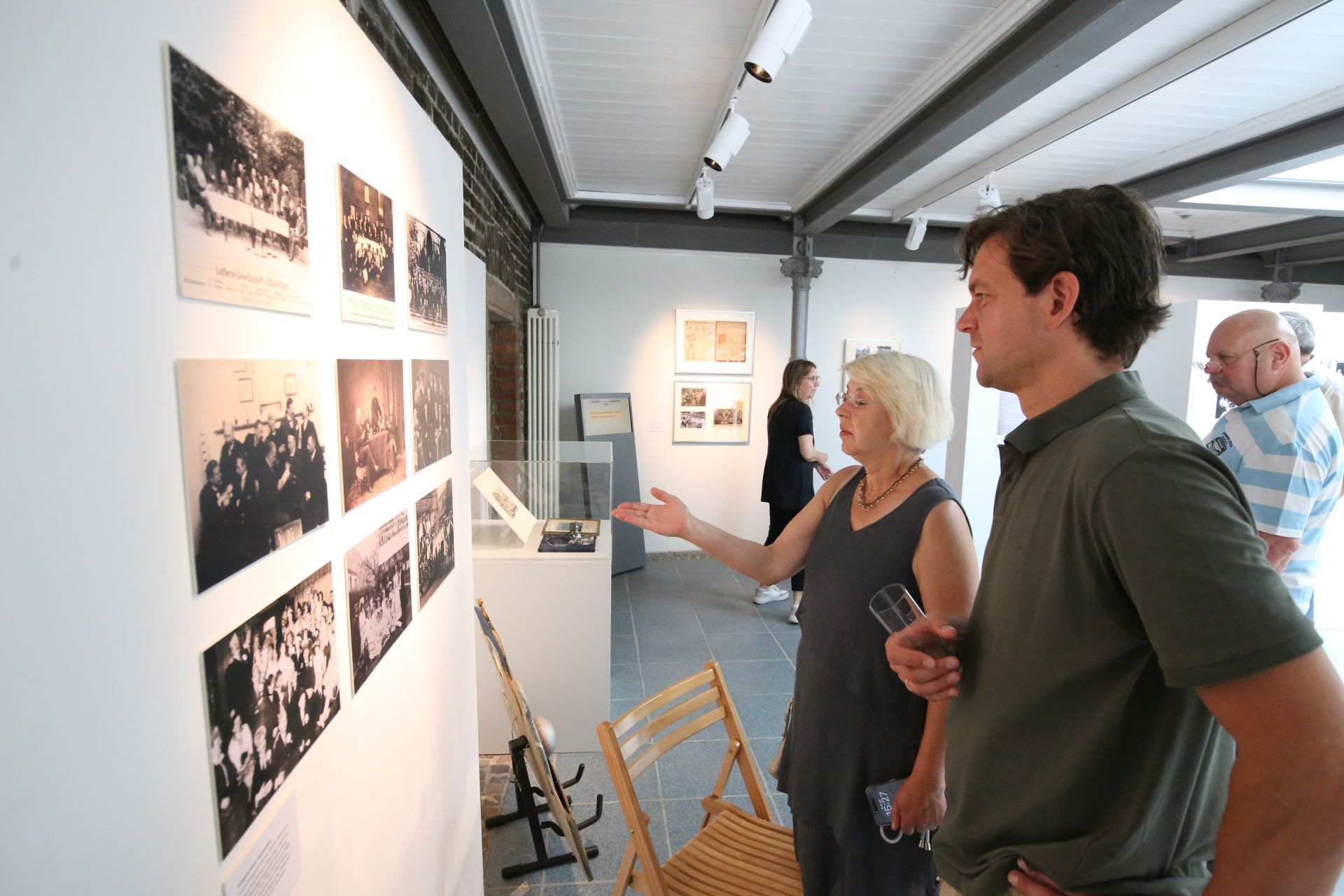 Ein Mann und eine Frau betrachten historische Schwarz-Weiß-Fotos in einer Ausstellung.